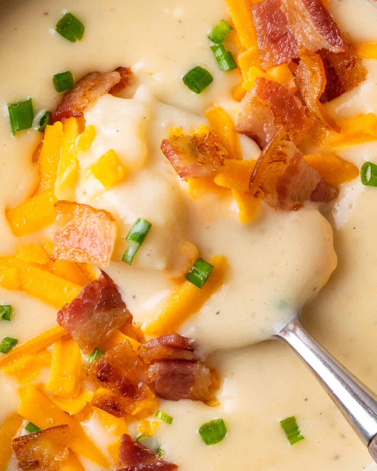 Este ¡La fácil sopa instantánea de papas está lista en minutos! Una receta de sopa sedosa, cremosa y nutritiva cargada de queso derretido y verduras. Cerca de una cucharada de sopa de patata adornada con tocino, queso rallado y cebollino.