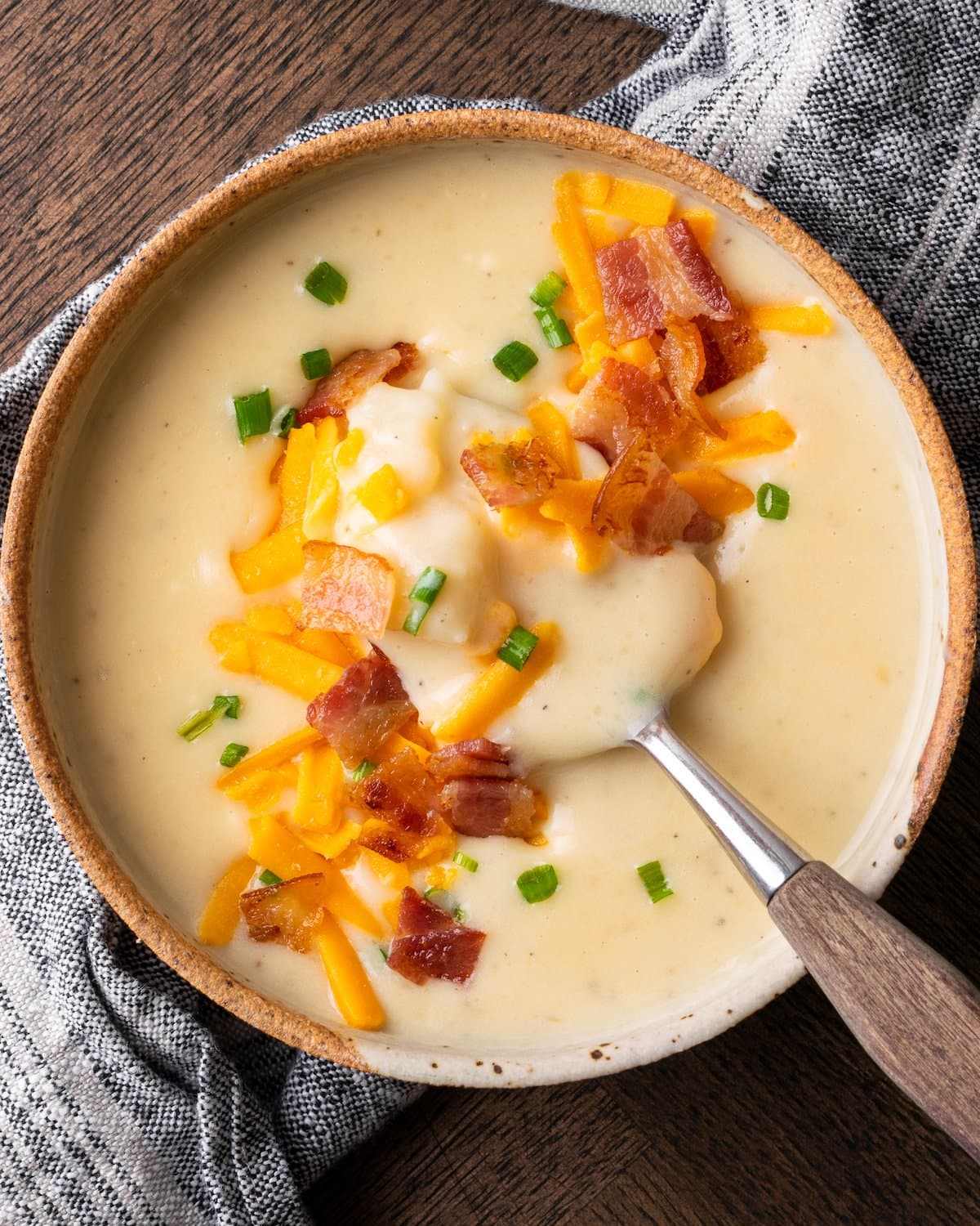¡Esta sencilla sopa instantánea de papas está lista en minutos! Una receta de sopa sedosa, cremosa y nutritiva cargada de queso derretido y verduras. Vista superior de la sopa de patata Instant Pot adornada con tocino, queso y cebollino, con una cuchara.