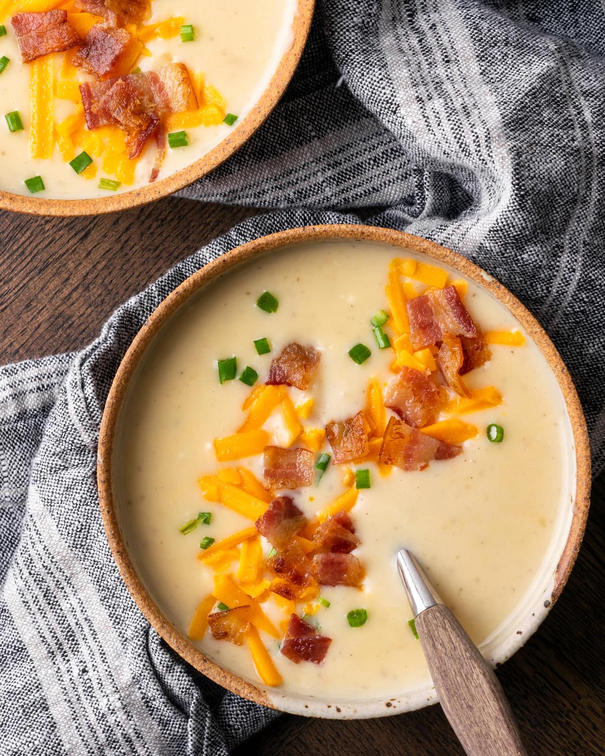 ¡Esta sencilla sopa instantánea de papas está lista en minutos! Una receta de sopa sedosa, cremosa y nutritiva cargada de queso derretido y verduras. Vista superior de dos tazones uno al lado del otro de sopa de papa Instant Pot cargada cubierta con queso rallado, trocitos de tocino y cebollín.