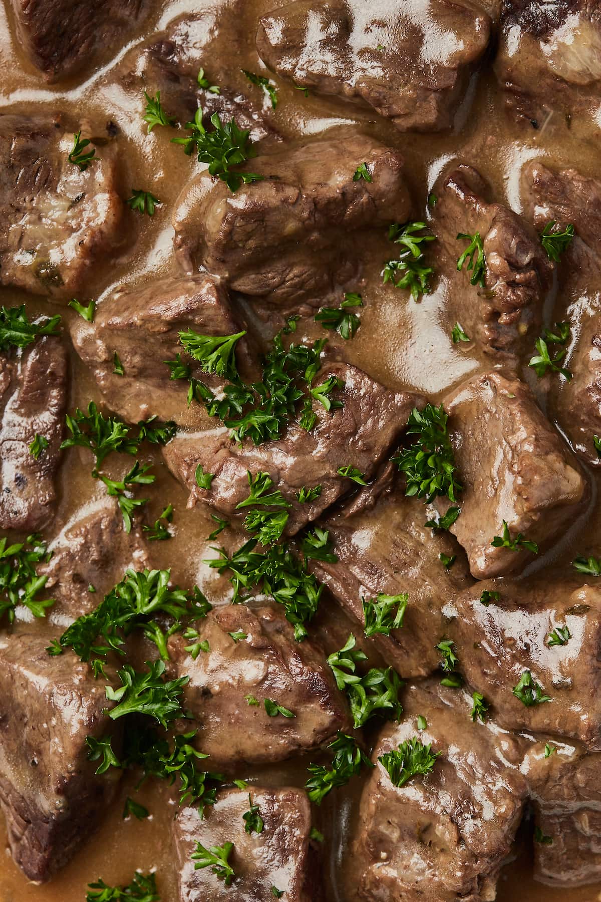 Primer plano de carne de res en cubos Instant Pot empapada en salsa y adornada con perejil fresco picado.