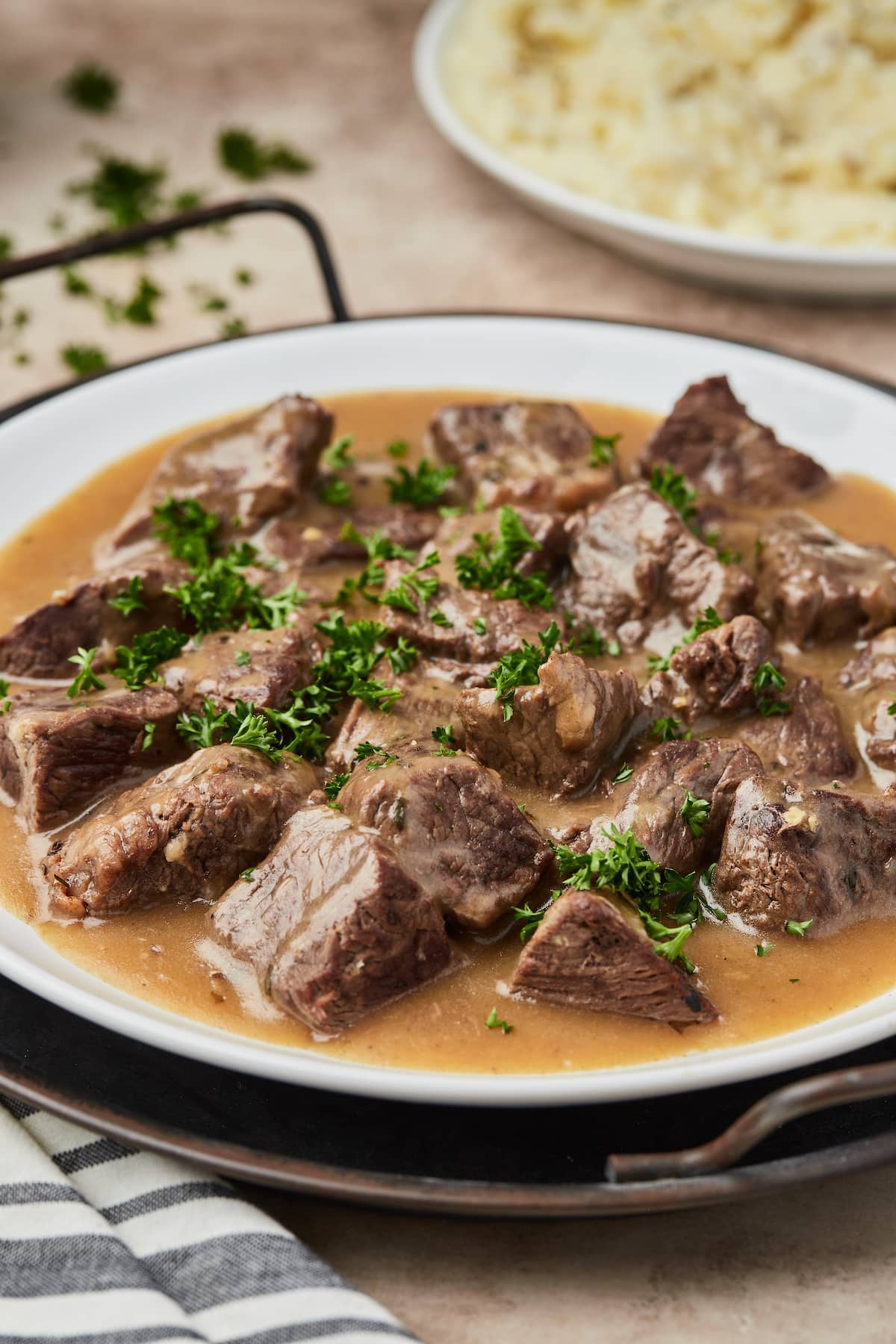 Ternera en cubos cubierta con salsa en un plato redondo adornado con perejil verde.