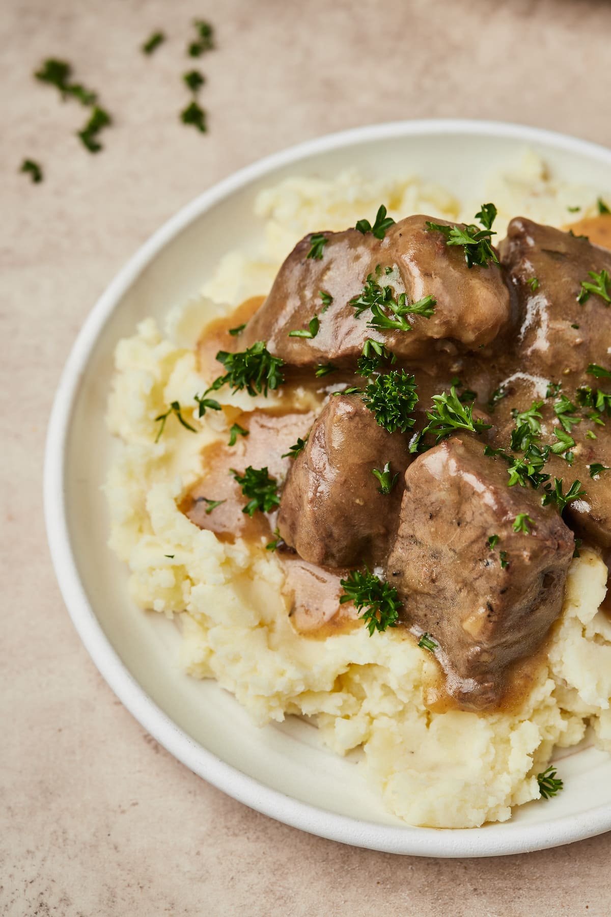 Carne de res en cubos Instant Pot y salsa servida sobre una cama de puré de papas en un plato.