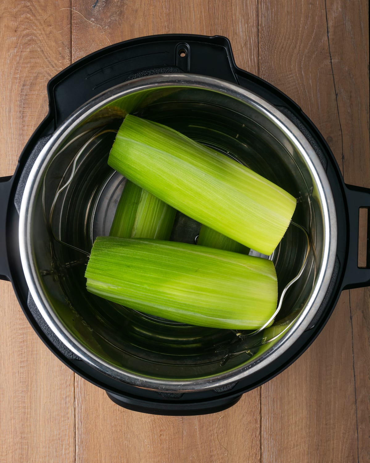 Instant Pot Corn on the Cob es, con mucho, la forma más fácil de disfrutar maíz fresco en minutos. Una guarnición fresca de verano cubierta con mantequilla de hierbas casera. Vista superior de mazorcas de maíz con cáscara dentro de una olla instantánea.