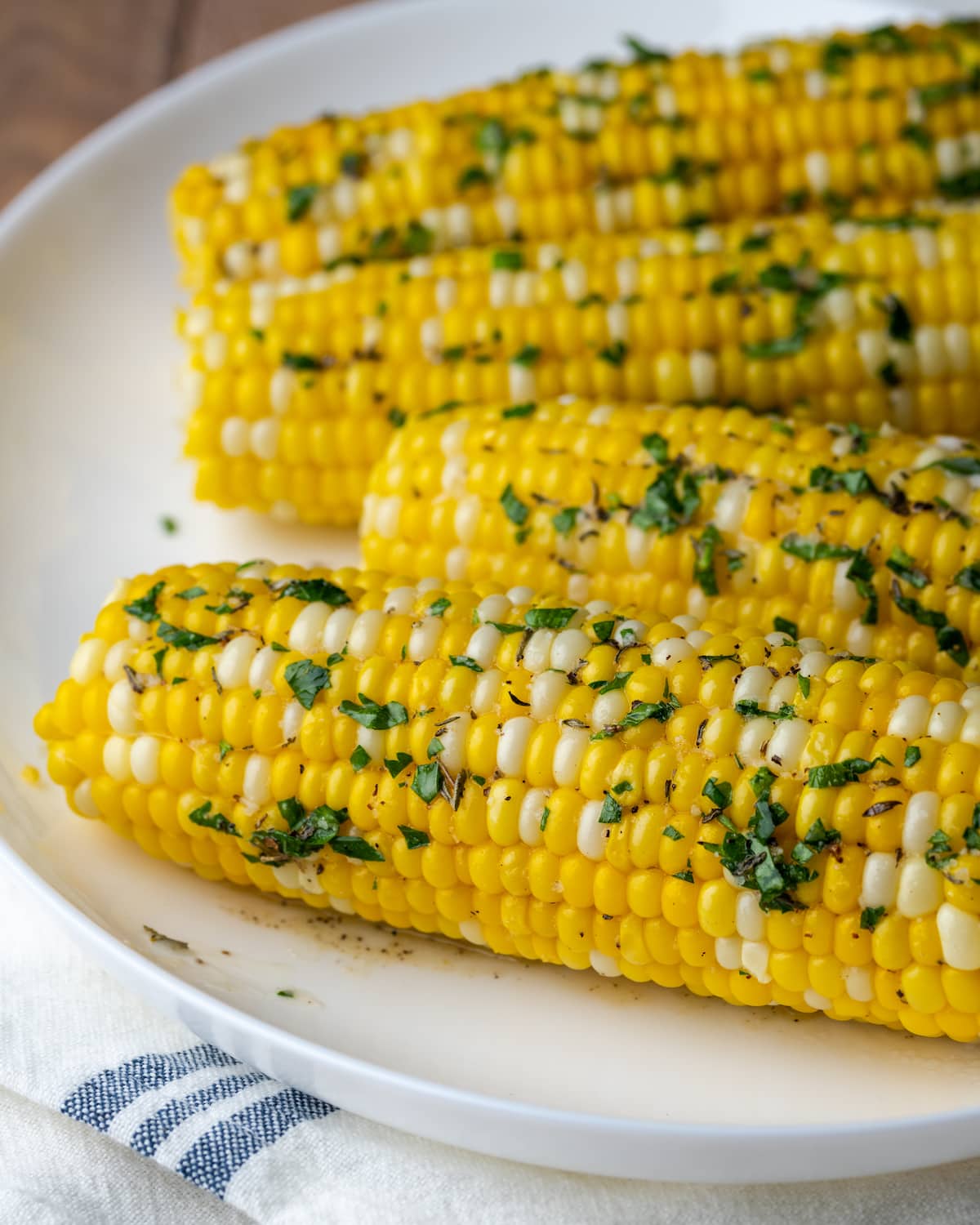Instant Pot Corn on the Cob es, con mucho, la forma más fácil de disfrutar maíz fresco en minutos. Una guarnición fresca de verano cubierta con mantequilla de hierbas casera. Maíz en la mazorca cubierto con mantequilla de hierbas en un plato blanco.