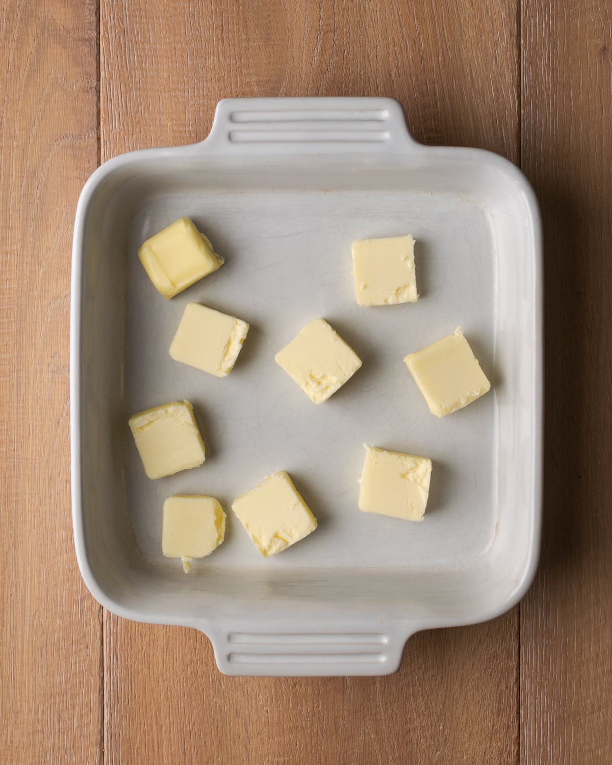 ¡Estas celestiales galletas Butter Swim se hornean doradas en mantequilla para obtener una textura increíblemente suave, húmeda y lista para rebanar! Vista superior de cubos de mantequilla en una cacerola cuadrada.