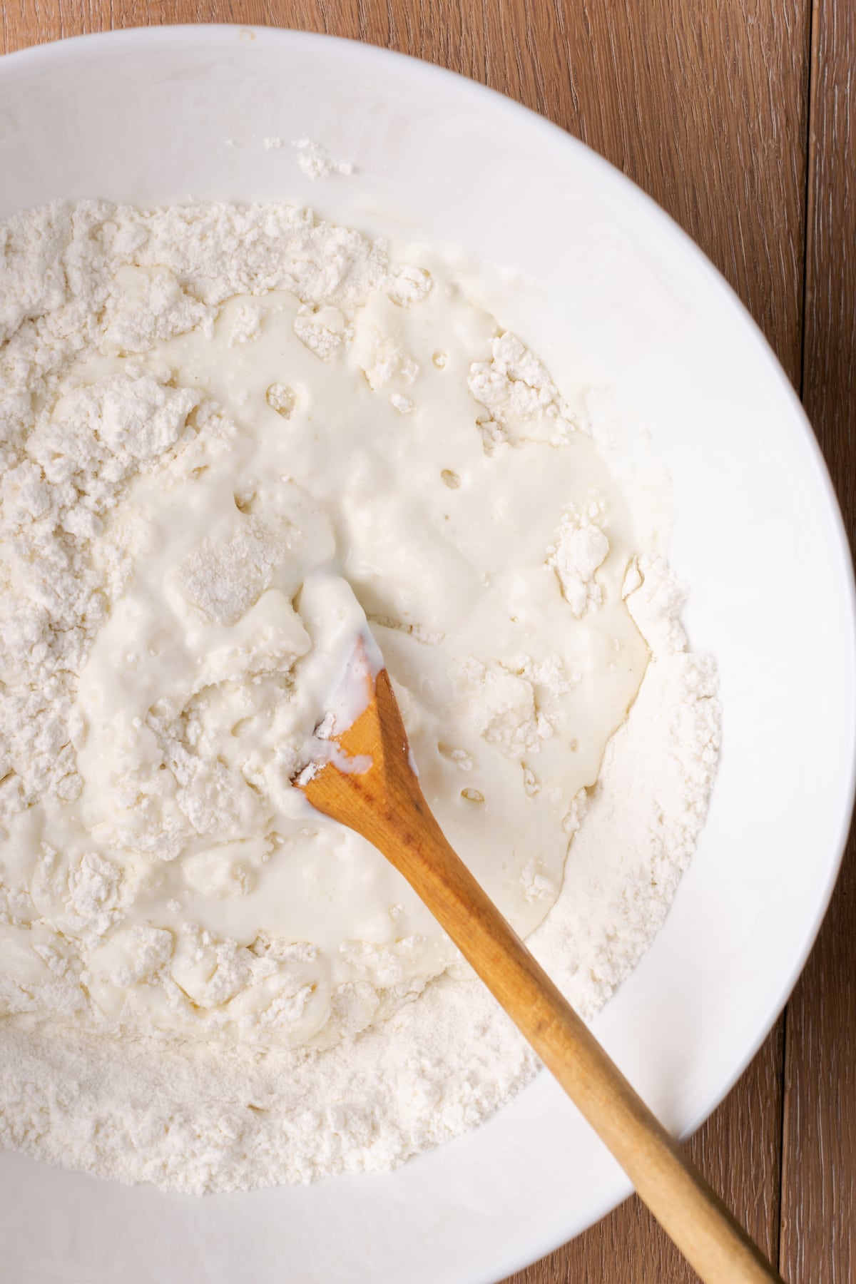 ¡Estas celestiales galletas Butter Swim se hornean doradas en mantequilla para obtener una textura increíblemente suave, húmeda y lista para rebanar! Primer plano de suero de leche combinado con ingredientes secos en un recipiente con una cuchara de madera.