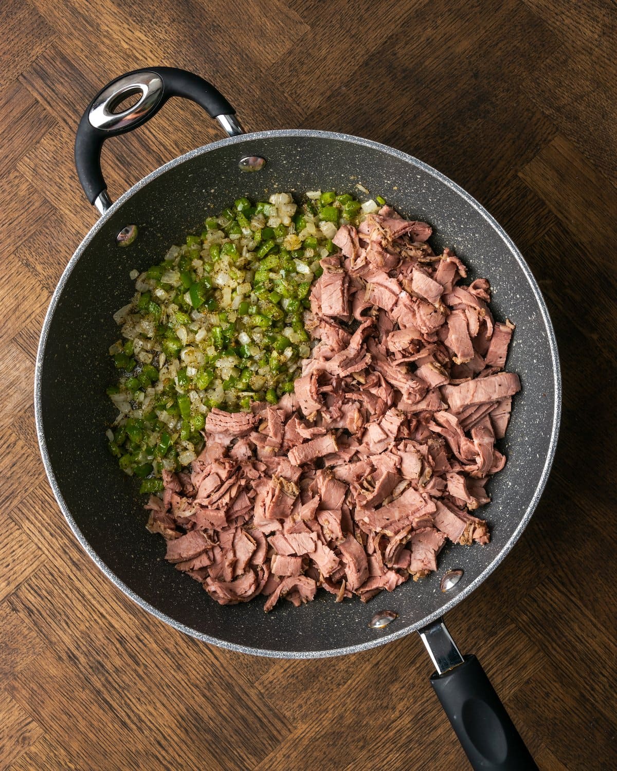 Carne asada en rodajas agregada a una sartén con cebollas y pimientos salteados en cubitos.