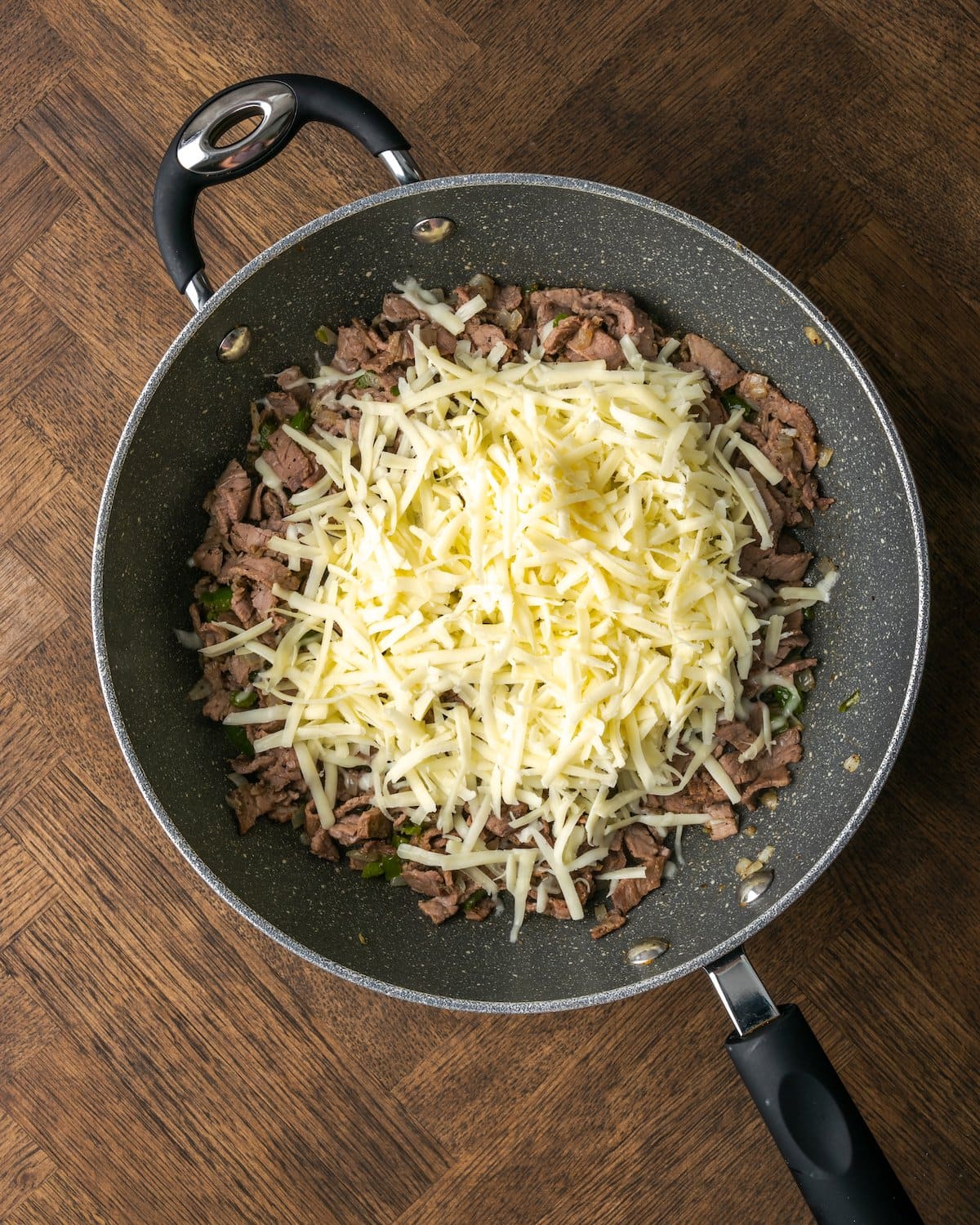 Queso rallado agregado a una sartén con la mezcla de bistec con queso Philly.