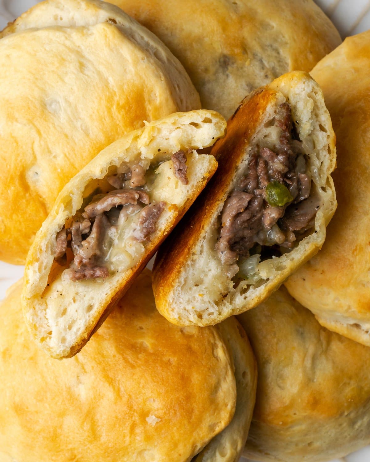 Una galleta rellena de bistec con queso Philly cortada por la mitad, rodeada de más galletas rellenas.