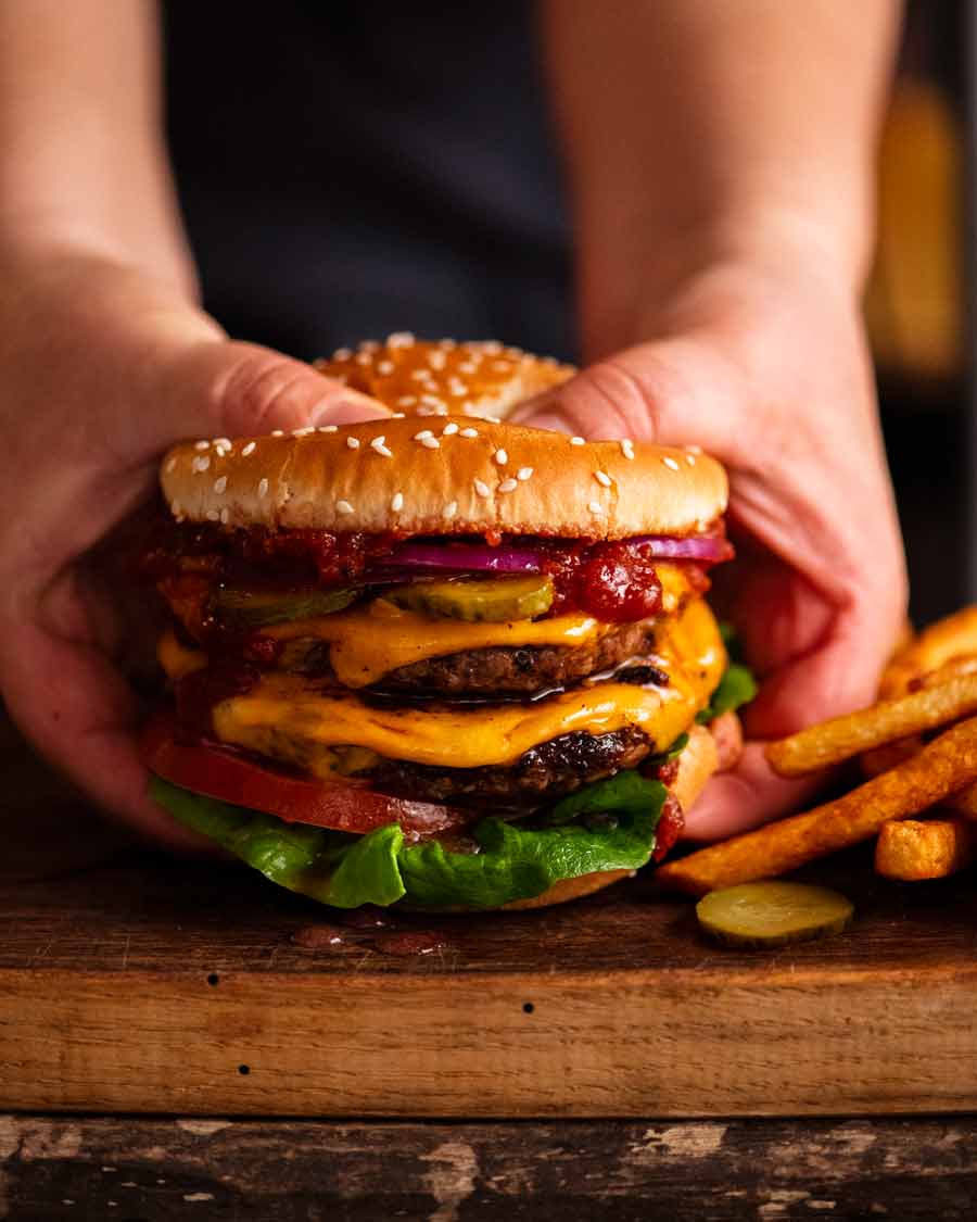 Mano que sostiene la hamburguesa doble con queso