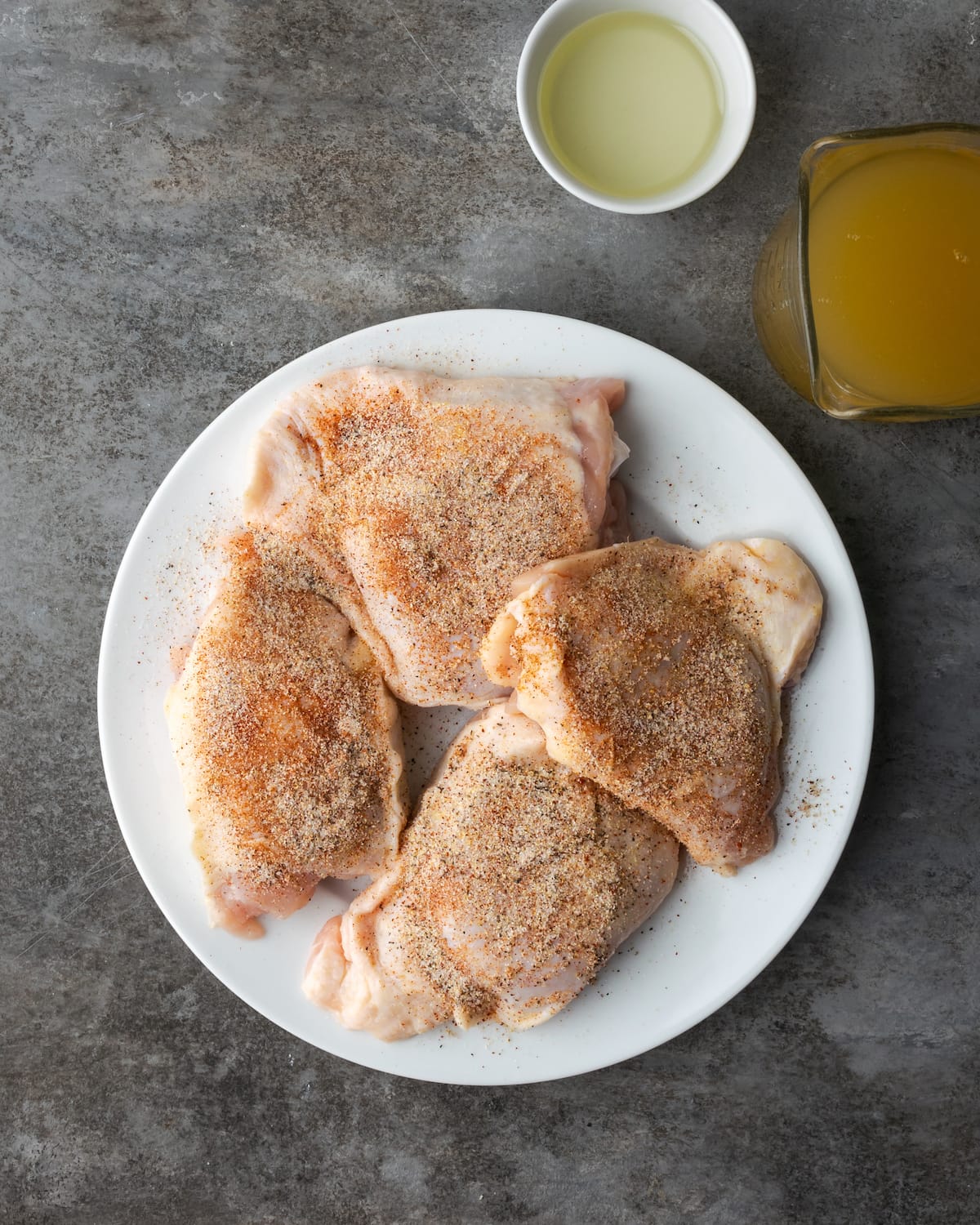 Vista superior de muslos de pollo crudos sazonados en un plato blanco.
