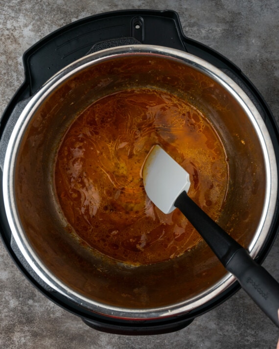 Se usa una espátula para aflojar los trozos de pollo chamuscados del fondo de la olla instantánea.