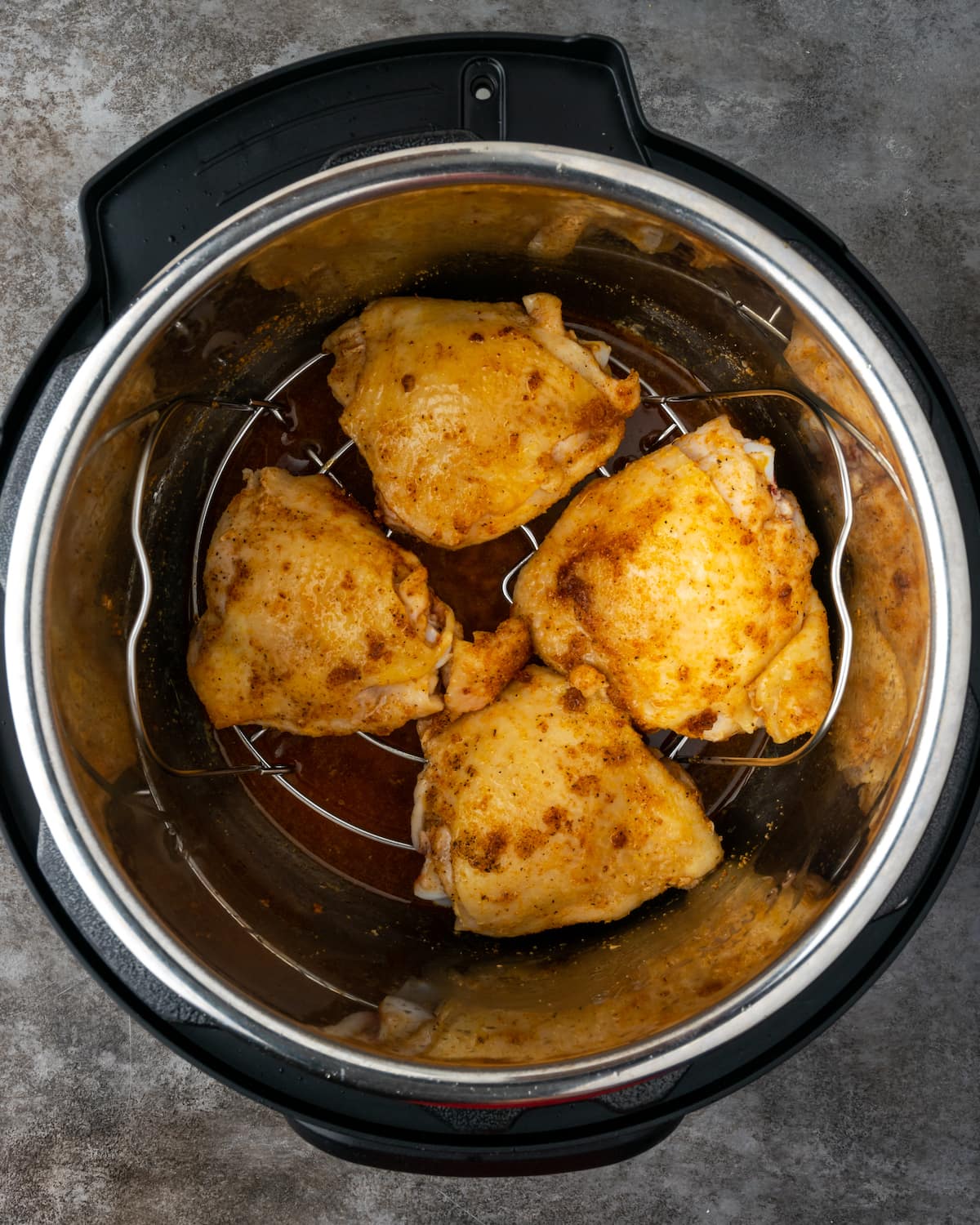Pechugas de pollo en un salvamanteles dentro de la olla instantánea, encima del caldo.