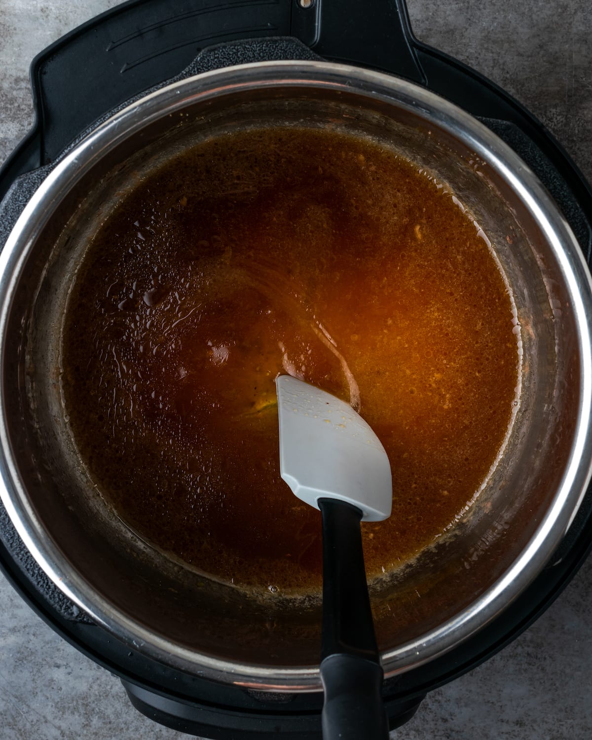 Se usa una espátula para revolver el caldo de res en el fondo de Instant Pot.