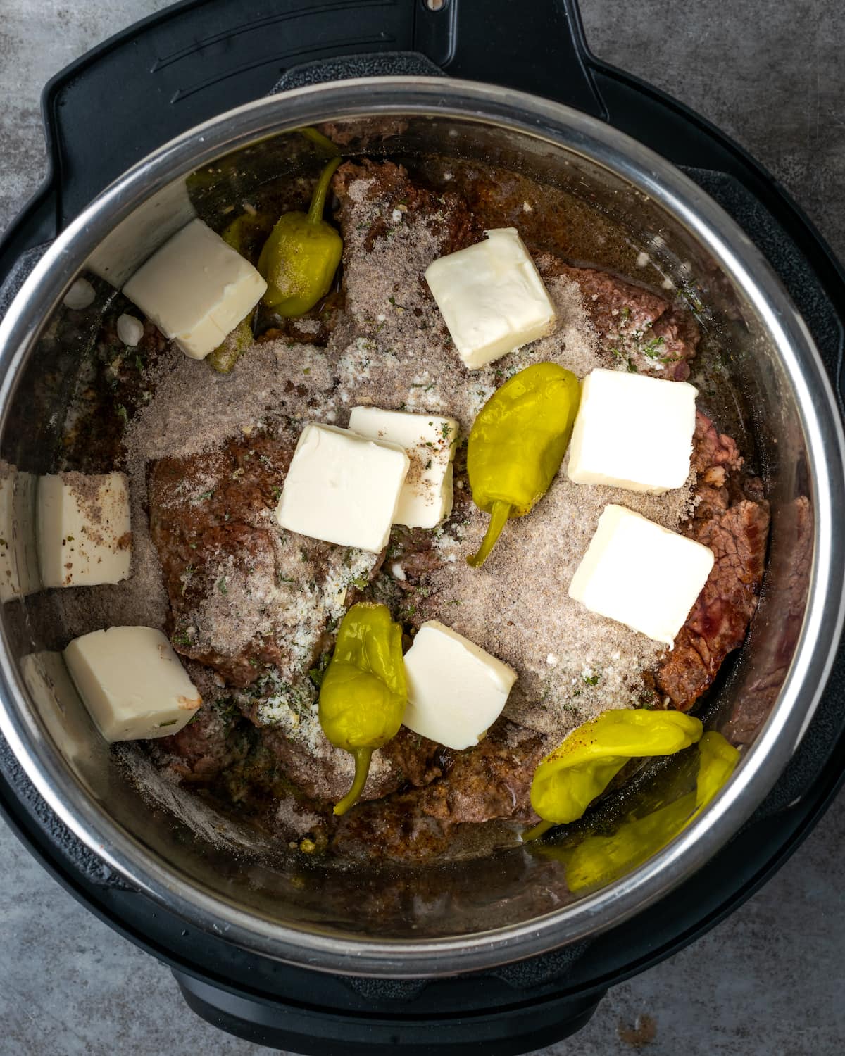 Se agregan condimentos, mezcla de salsa, pepperoncini y un poco de mantequilla sobre la carne dentro de Instant Pot.
