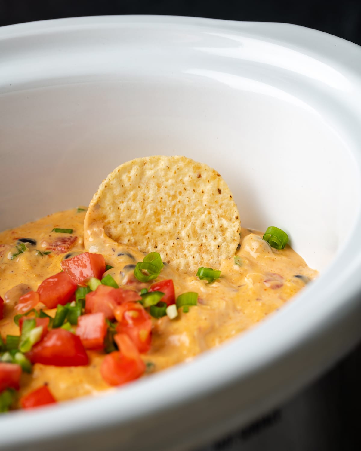 Primer plano de un chip de nacho sumergido en salsa de nacho de pollo con queso dentro de una olla de barro.