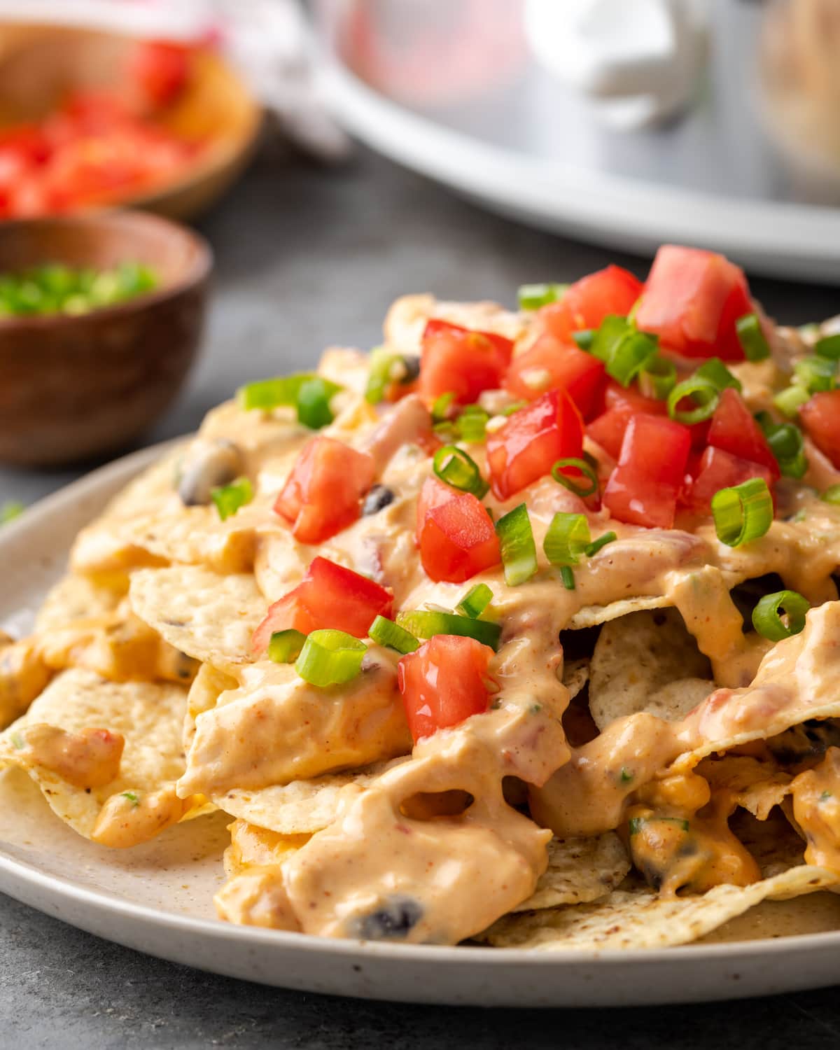 Un plato de nachos de pollo cubierto con salsa de nacho de pollo Crock Pot, adornado con tomates cortados en cubitos y jalapeños.