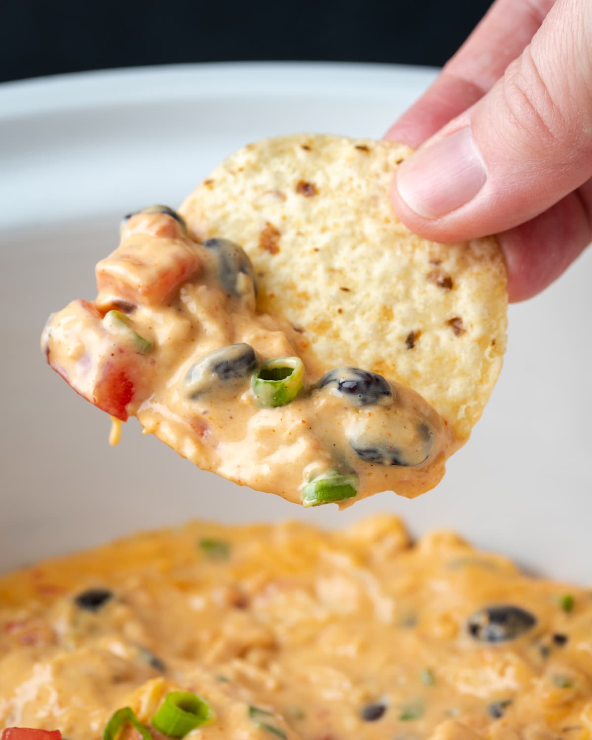 Una mano que sostiene un chip sumergido en salsa de nacho de pollo Crock Pot.