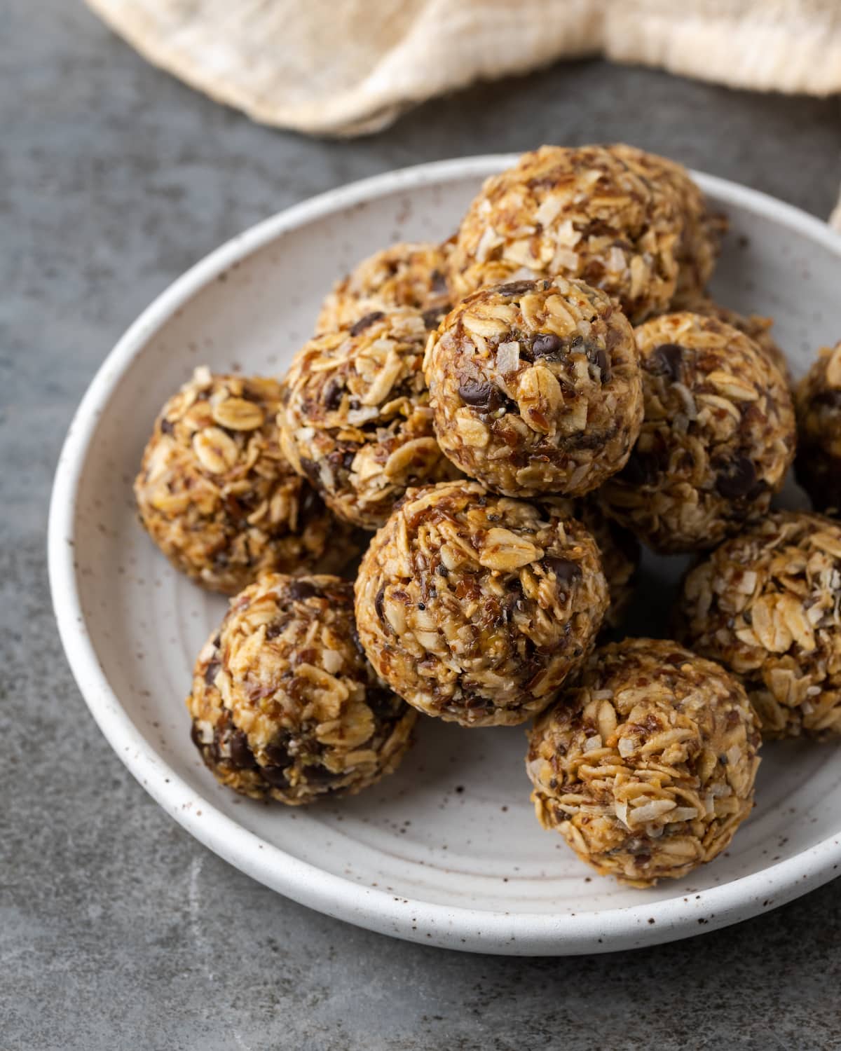 ¡Estas mordidas energéticas sin hornear con mantequilla de maní y chocolate toman solo unos minutos para prepararse! Una receta fácil de bolitas de proteínas para un refrigerio saludable. Bocados energéticos sin hornear apilados en un plato blanco.