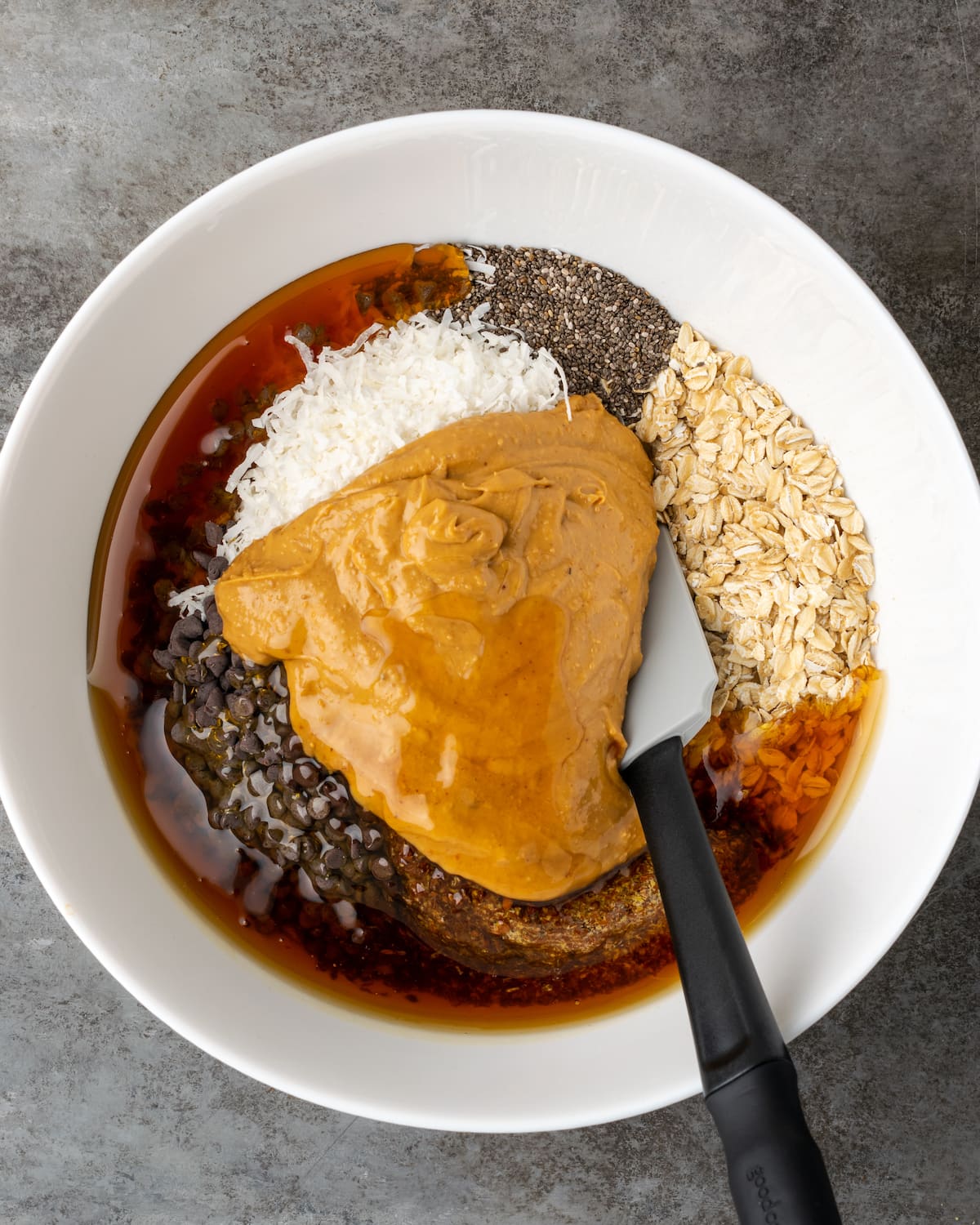 ¡Estas mordidas energéticas sin hornear con mantequilla de maní y chocolate toman solo unos minutos para prepararse! Una receta fácil de bolitas de proteínas para un refrigerio saludable. Los ingredientes para los bocados energéticos de mantequilla de maní con chocolate combinados en un tazón blanco.