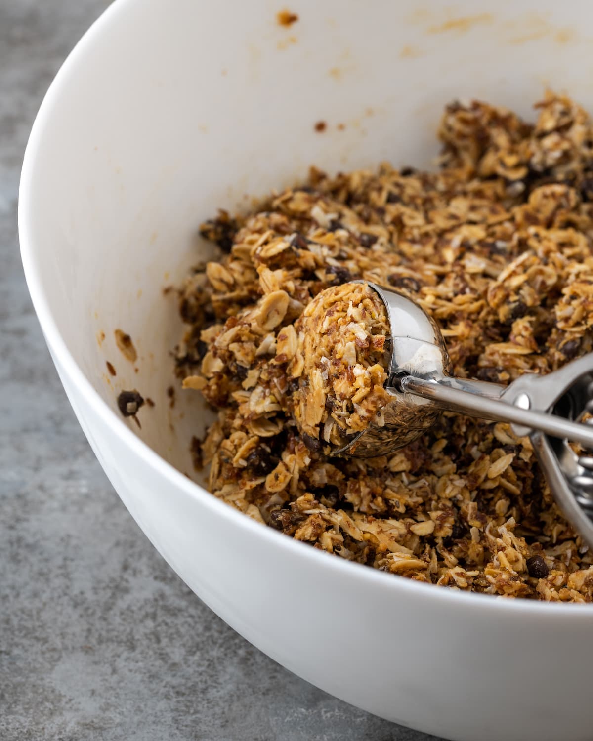 ¡Estas mordidas energéticas sin hornear con mantequilla de maní y chocolate toman solo unos minutos para prepararse! Una receta fácil de bolitas de proteínas para un refrigerio saludable. Se usa una cuchara para galletas para repartir la mezcla energética de mantequilla de maní con chocolate de un tazón blanco.