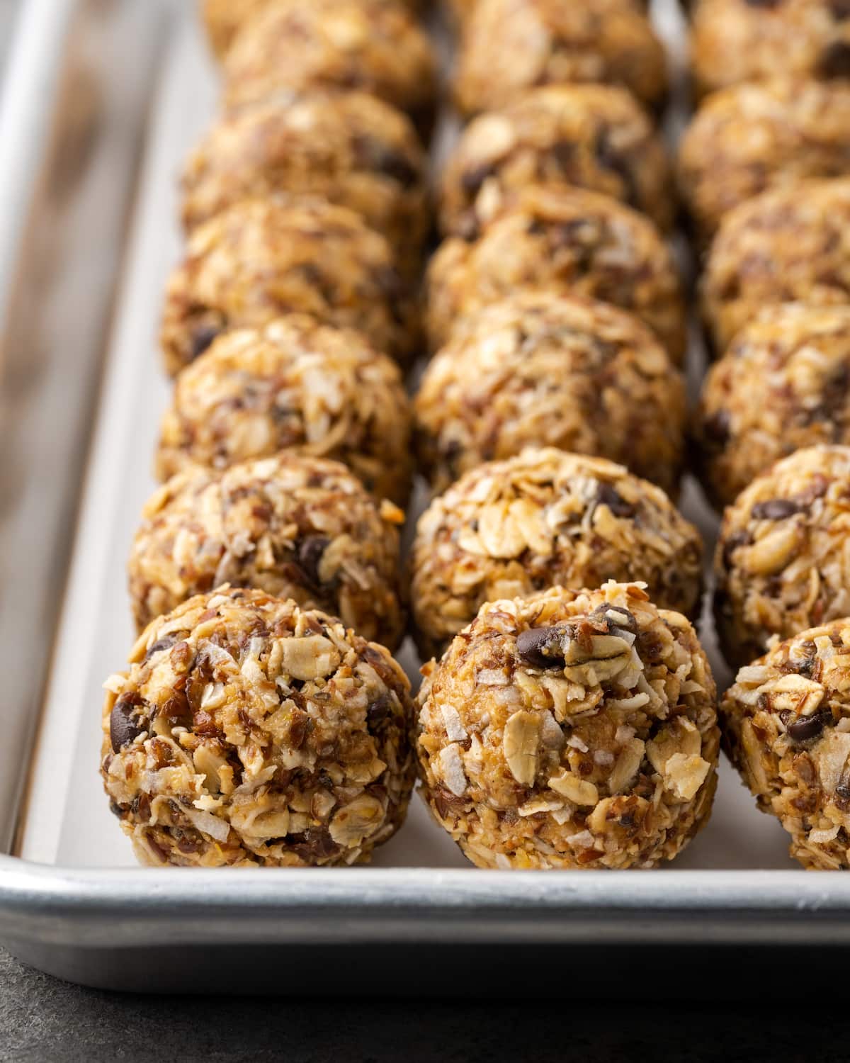 ¡Estas mordidas energéticas sin hornear con mantequilla de maní y chocolate toman solo unos minutos para prepararse! Una receta fácil de bolitas de proteínas para un refrigerio saludable. Filas de bocados energéticos de mantequilla de maní con chocolate sin hornear en una bandeja para hornear.
