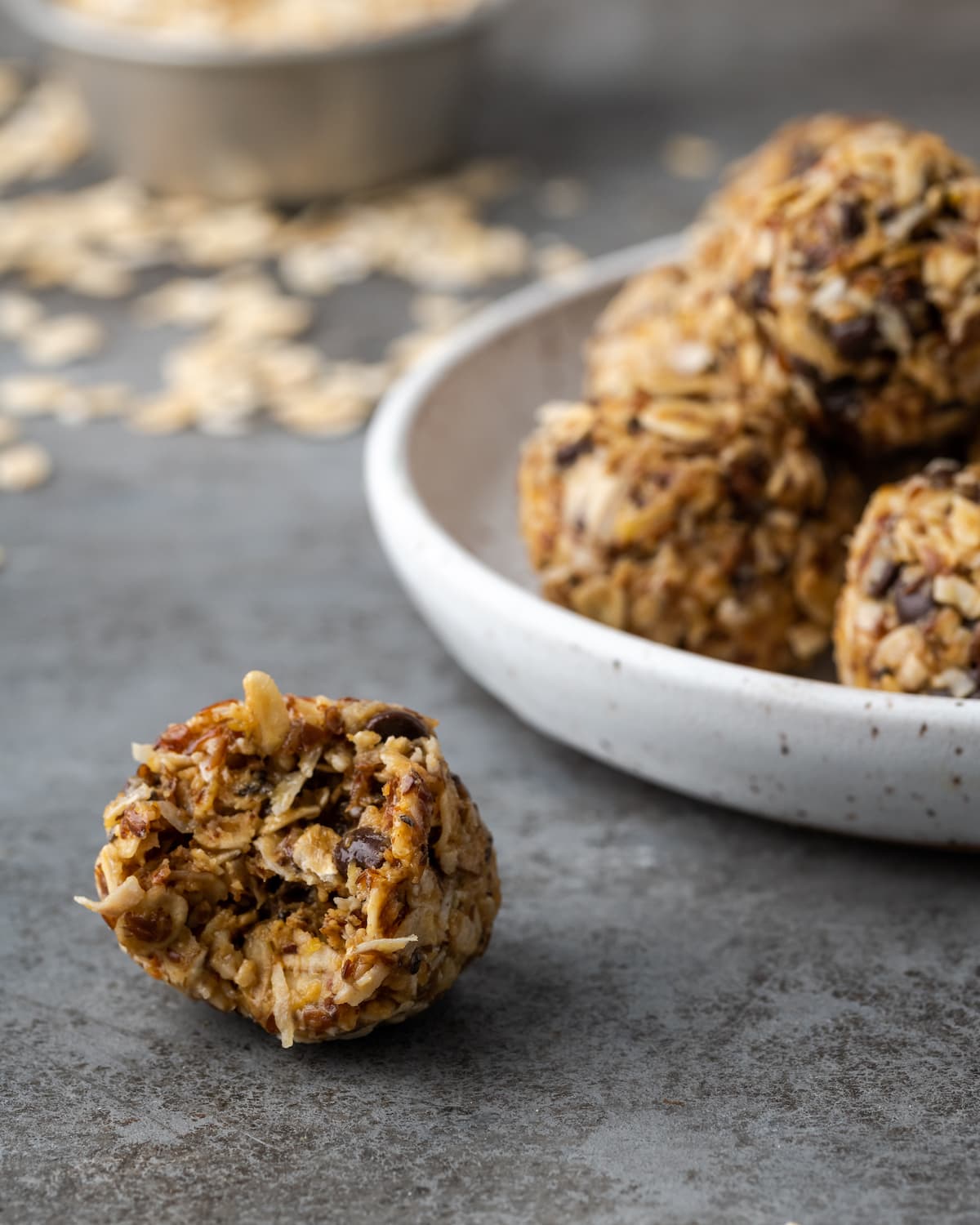 ¡Estas mordidas energéticas sin hornear con mantequilla de maní y chocolate toman solo unos minutos para prepararse! Una receta fácil de bolitas de proteínas para un refrigerio saludable. Primer plano de un bocado energético al que le falta un bocado, junto a un plato de bocados energéticos.