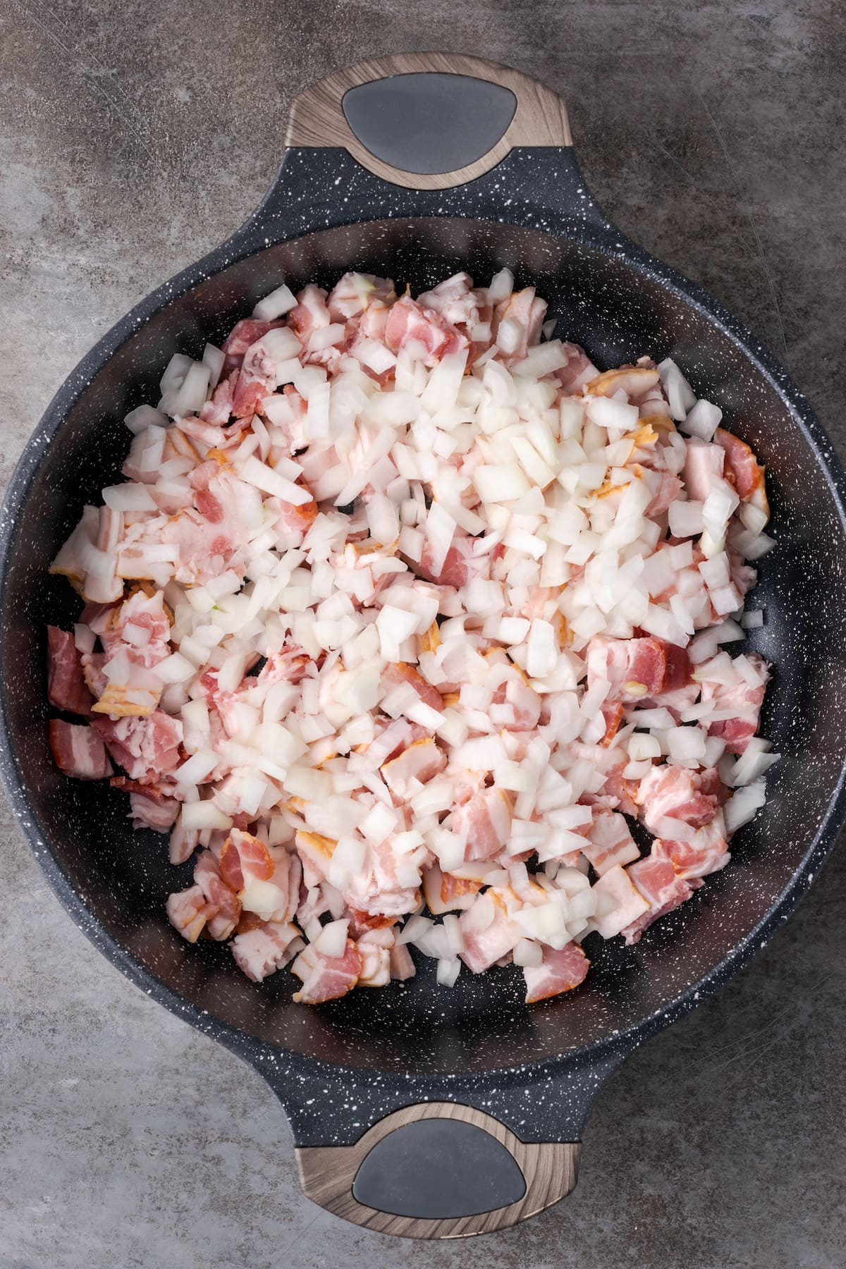 Cebolla picada y tocino en una sartén grande de hierro fundido.