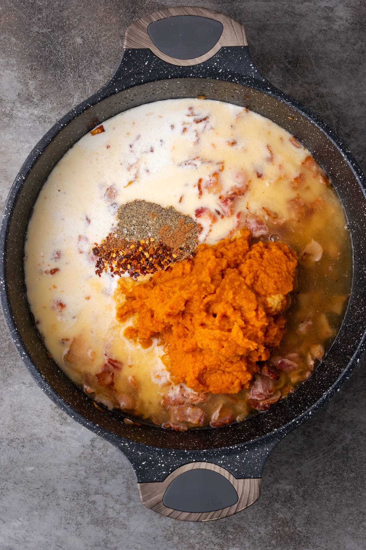 El puré de calabaza y el resto de los ingredientes de la salsa de calabaza se agregan a una sartén de hierro fundido con tocino y cebolla.