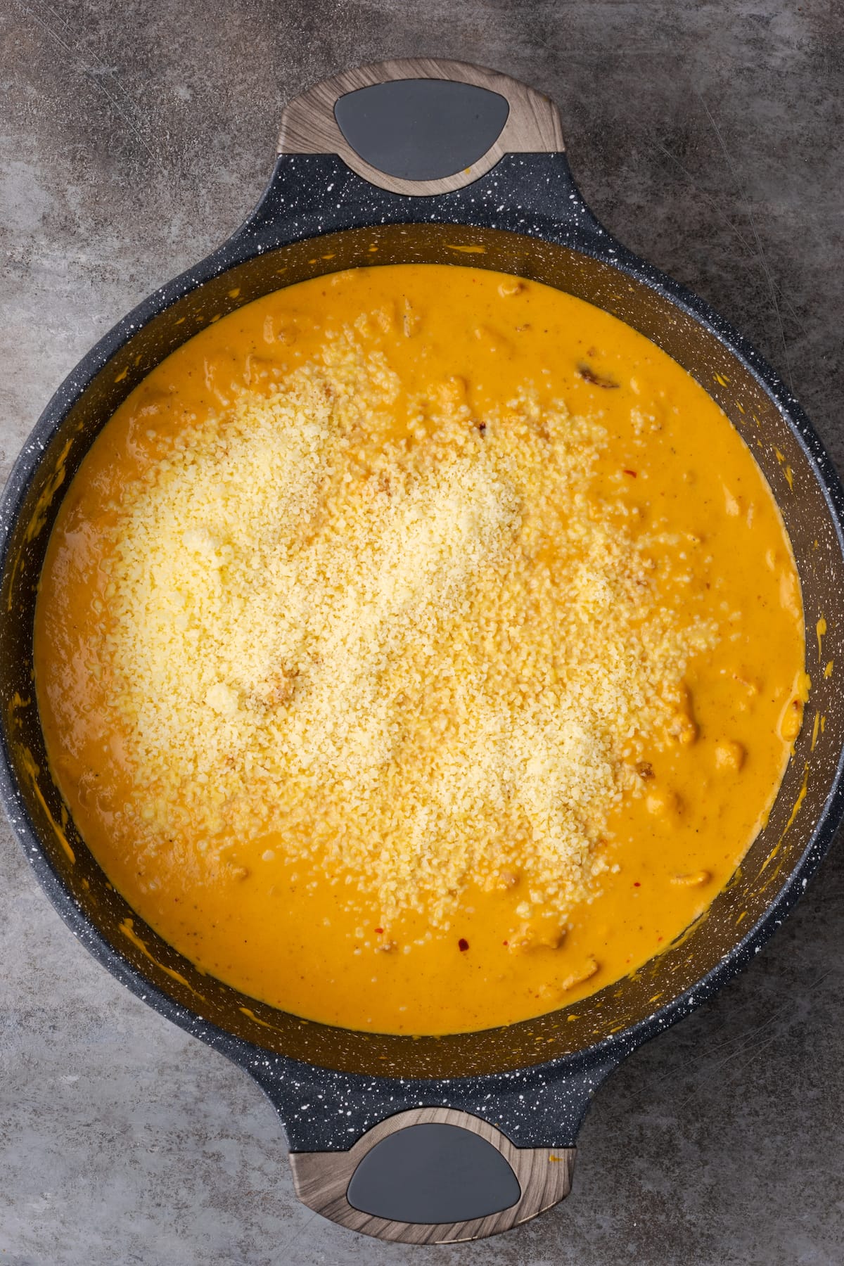 El queso parmesano se agrega a la salsa de crema de calabaza en una sartén de hierro fundido.