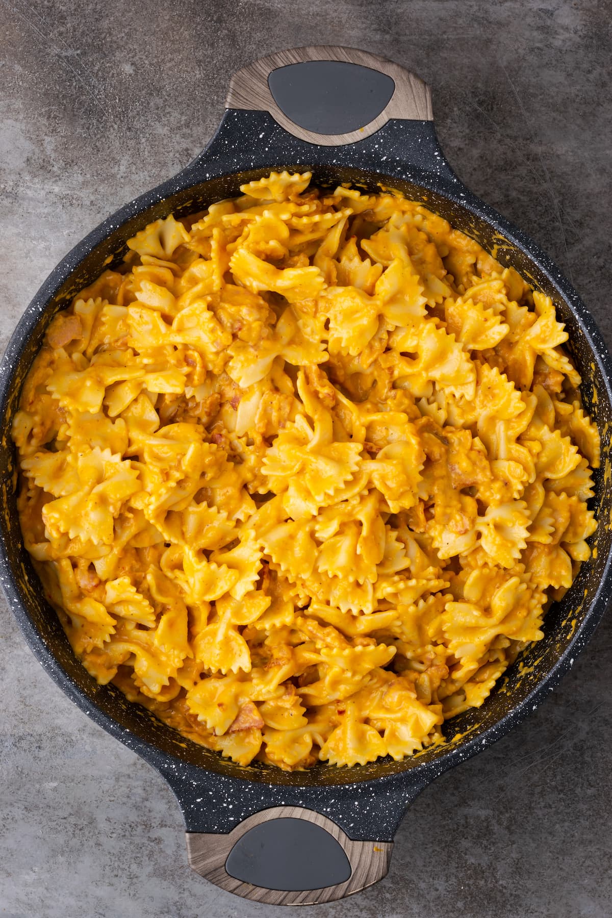 Pasta de calabaza terminada con tocino en una sartén grande de hierro fundido.