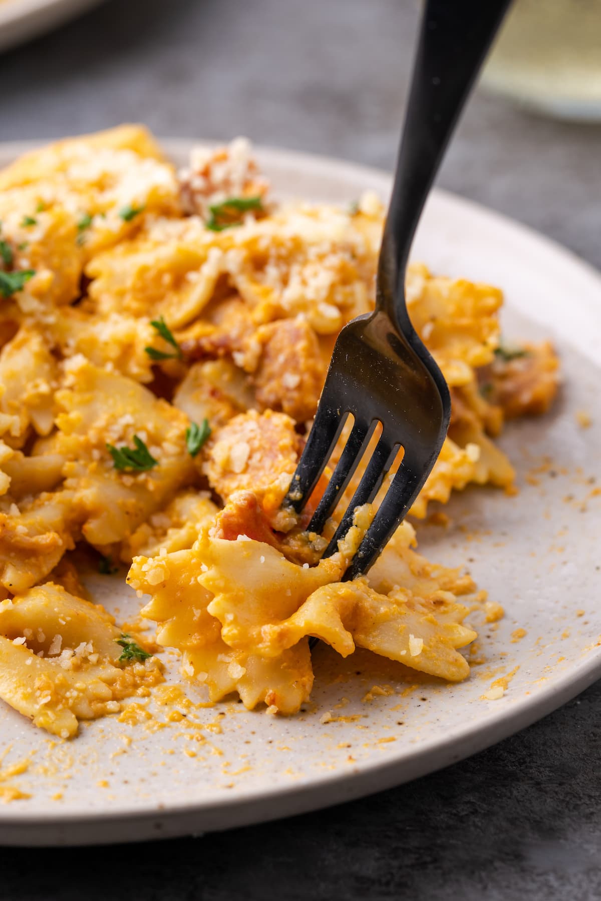 Un tenedor recoge un bocado de pasta de calabaza farfalle con tocino de un plato.
