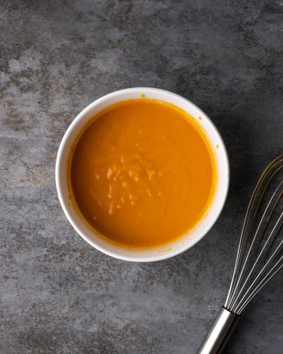 Los ingredientes húmedos para la masa de zapatero de calabaza combinados en un tazón blanco.