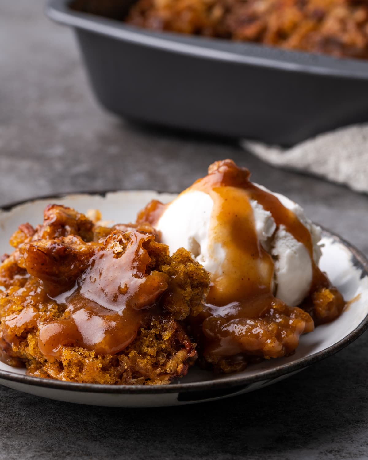 Una porción de zapatero de calabaza en un plato blanco cubierto con una bola de helado de vainilla y salsa de caramelo.