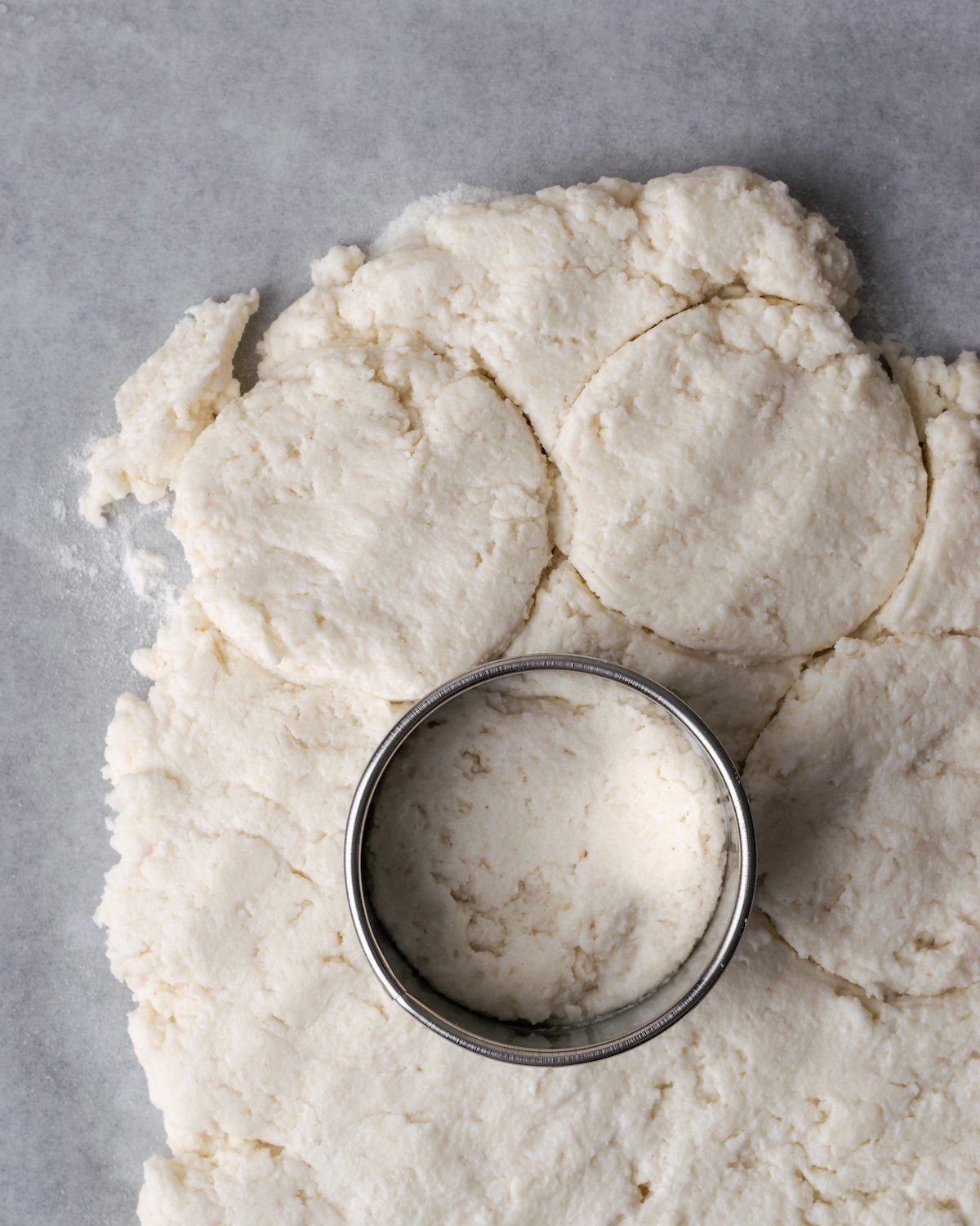 Un cortador de galletas colocado sobre masa de galletas aplanada, con círculos cortados de la masa.