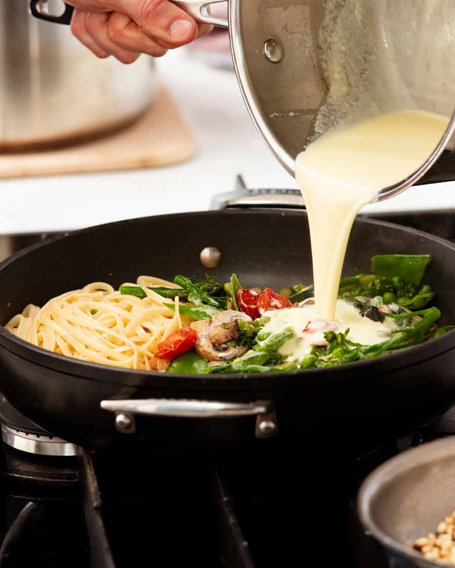 Verter salsa de crema sobre Pasta Primavera