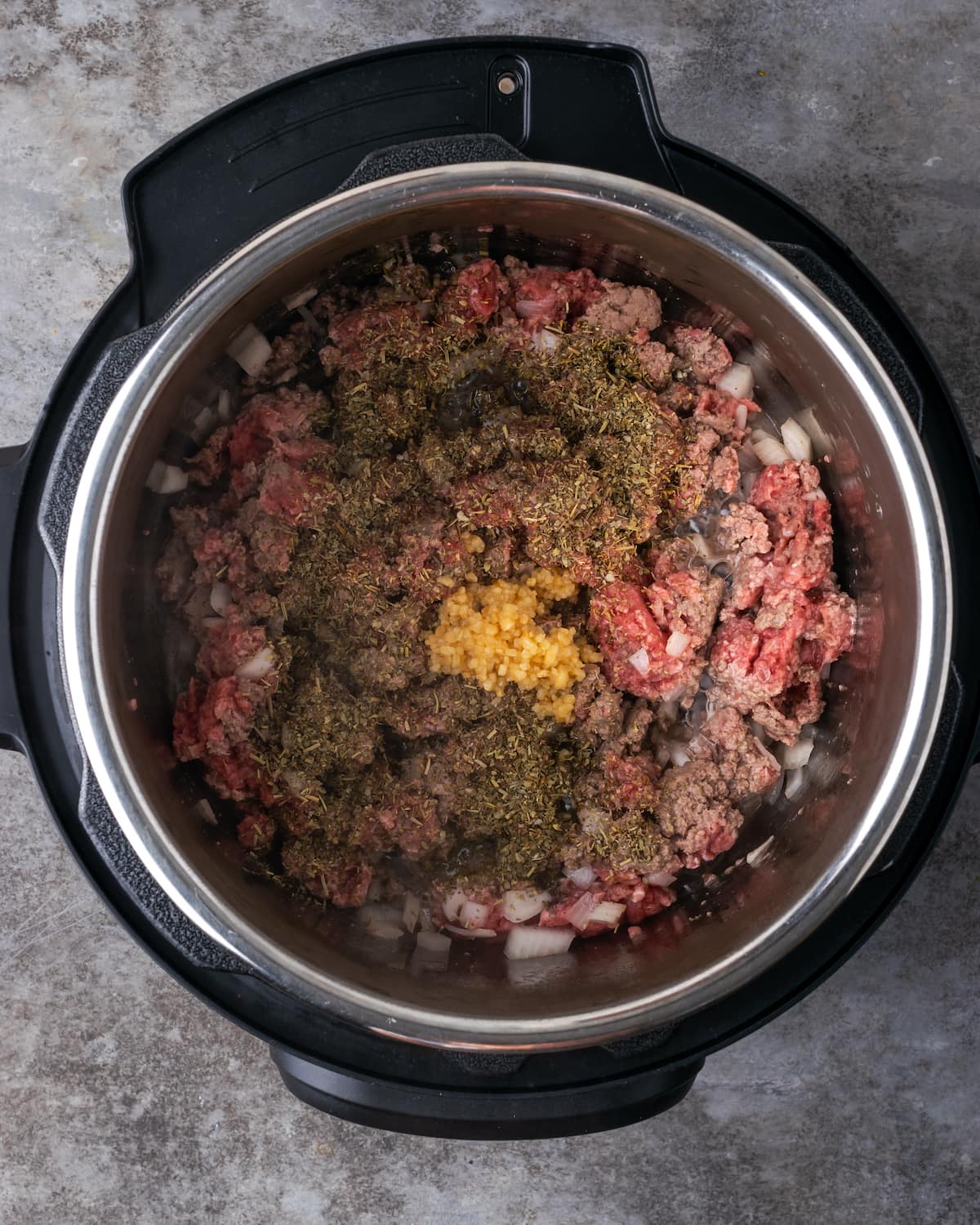 Vista aérea de la carne molida combinada con cebollas y condimentos en el fondo de la olla instantánea.