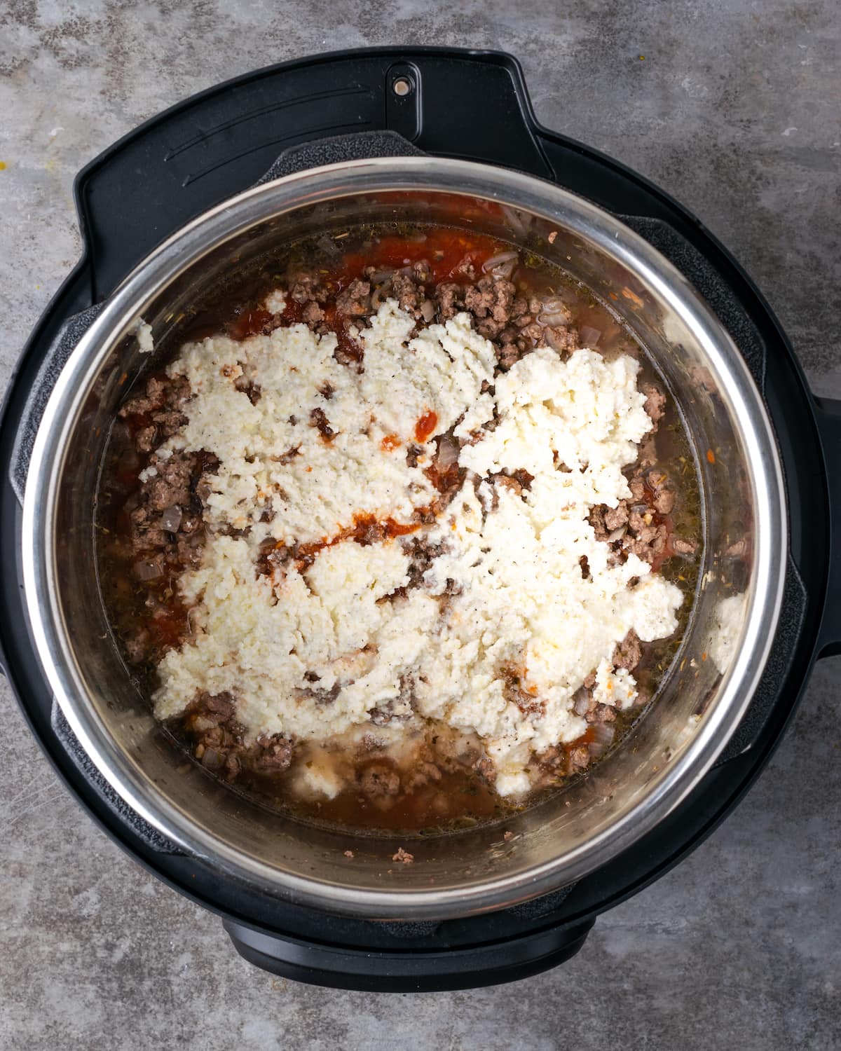 Vista aérea de la carne molida cubierta con marinara y queso ricotta dentro de la olla instantánea.