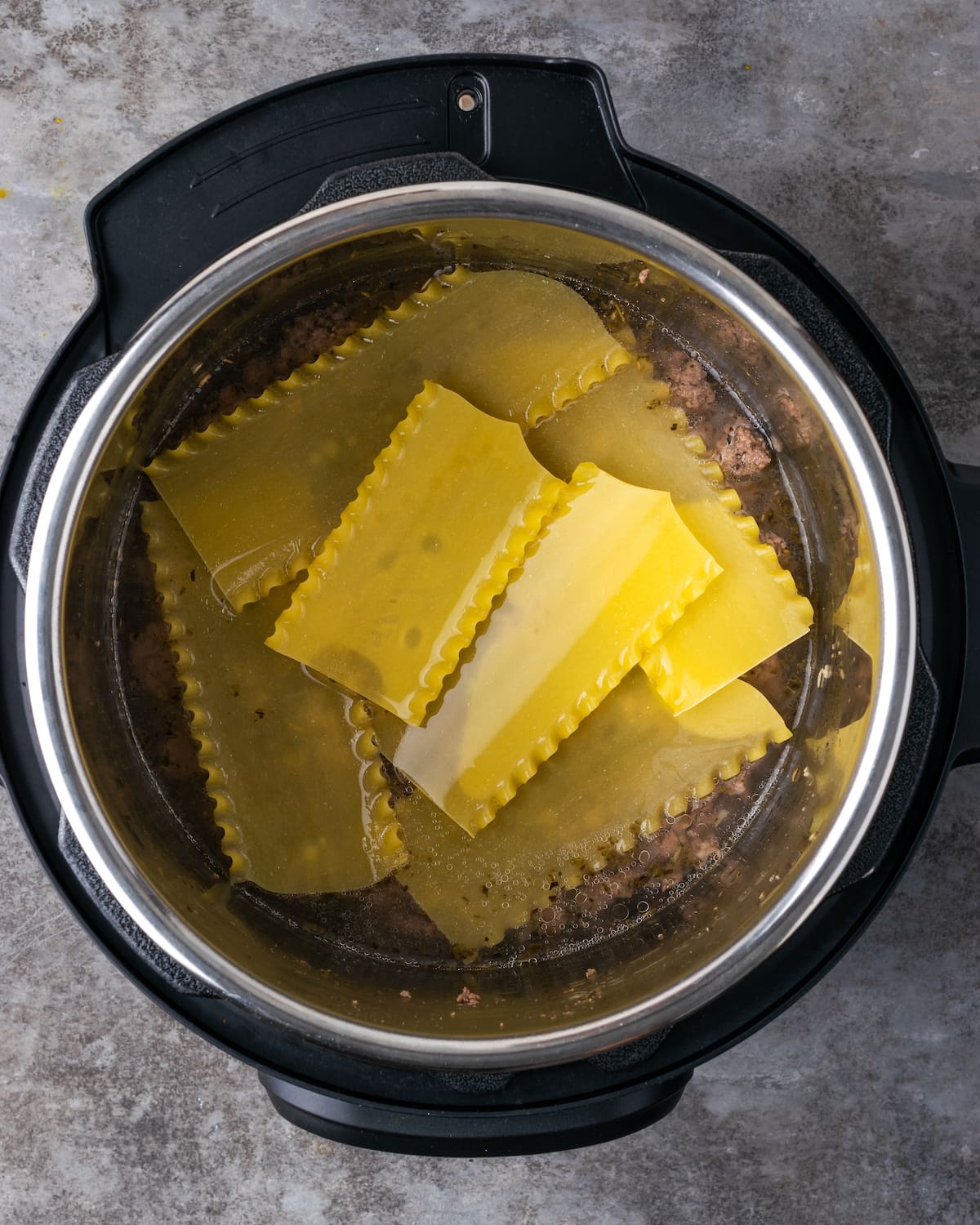 Vista aérea de la carne molida cubierta con la primera capa de fideos de lasaña dentro de la olla instantánea.