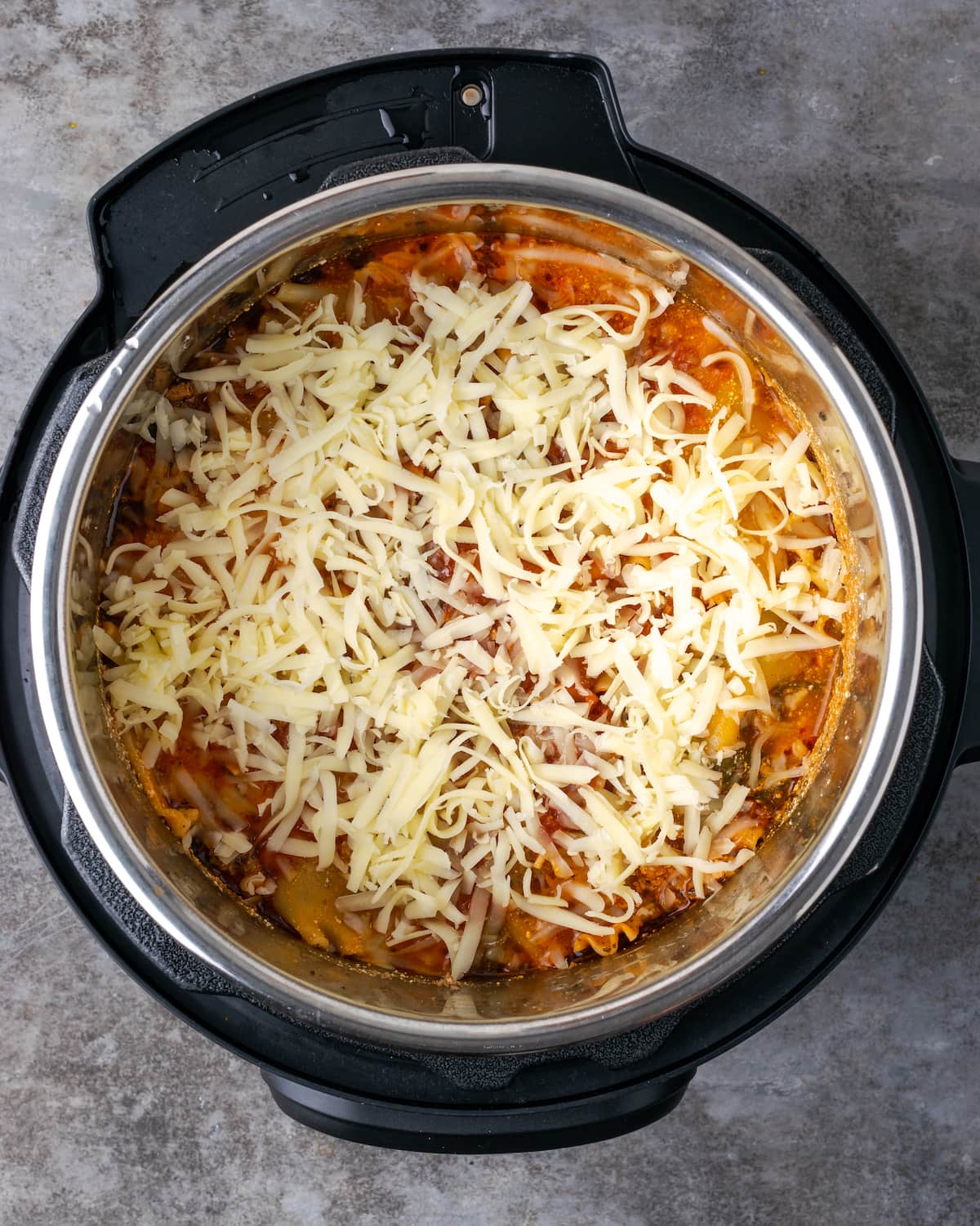 Vista superior de lasaña cocida Instant Pot cubierta con mozzarella rallada dentro de la olla.