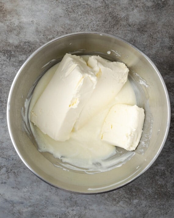 Los bloques de queso crema se agregan a un tazón con crema agria y azúcar para la masa de tarta de queso.