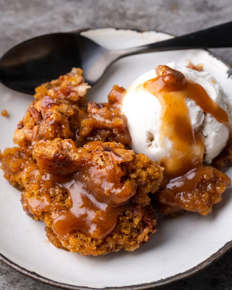 Una porción de zapatero de calabaza en un plato blanco cubierto con una bola de helado de vainilla y salsa de caramelo.