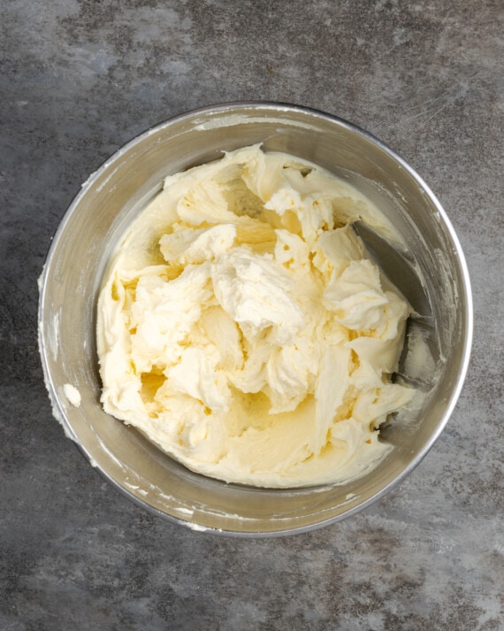 Esta receta de pastel Cannoli transforma un favorito de la panadería en un delicioso pastel de capas de vainilla. ¡Completa con relleno de mascarpone casero! Ingredientes de relleno de mascarpone combinados en un tazón de metal.