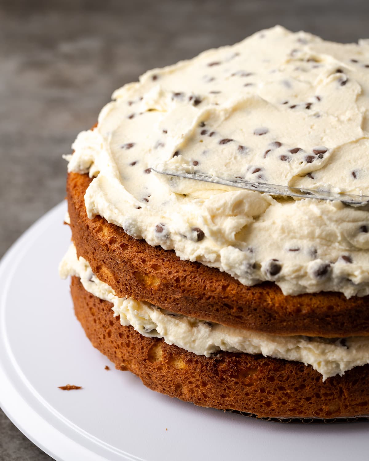 Esta receta de pastel Cannoli transforma un favorito de la panadería en un delicioso pastel de capas de vainilla. ¡Completa con relleno de mascarpone casero! Pastel de cannoli ensamblado y sin glasear que muestra las capas de pastel de vainilla y relleno de crema.