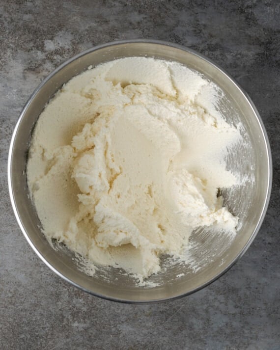 Esta receta de pastel Cannoli transforma un favorito de la panadería en un delicioso pastel de capas de vainilla. ¡Completa con relleno de mascarpone casero! Glaseado de vainilla en una mezcla de metales cuenco.