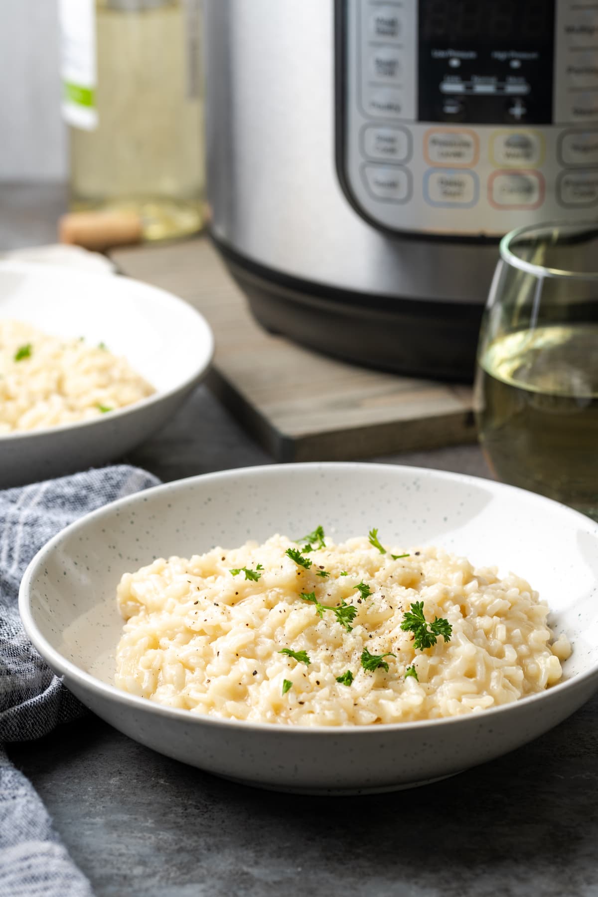 Esta receta de Instant Pot Risotto es un plato principal o guarnición fácil que es tan rico y cremoso como el risotto clásico, ¡y está listo en 30 minutos! Un tazón de cremoso risotto Instant Pot adornado con perejil fresco, con el Instant Pot de fondo.