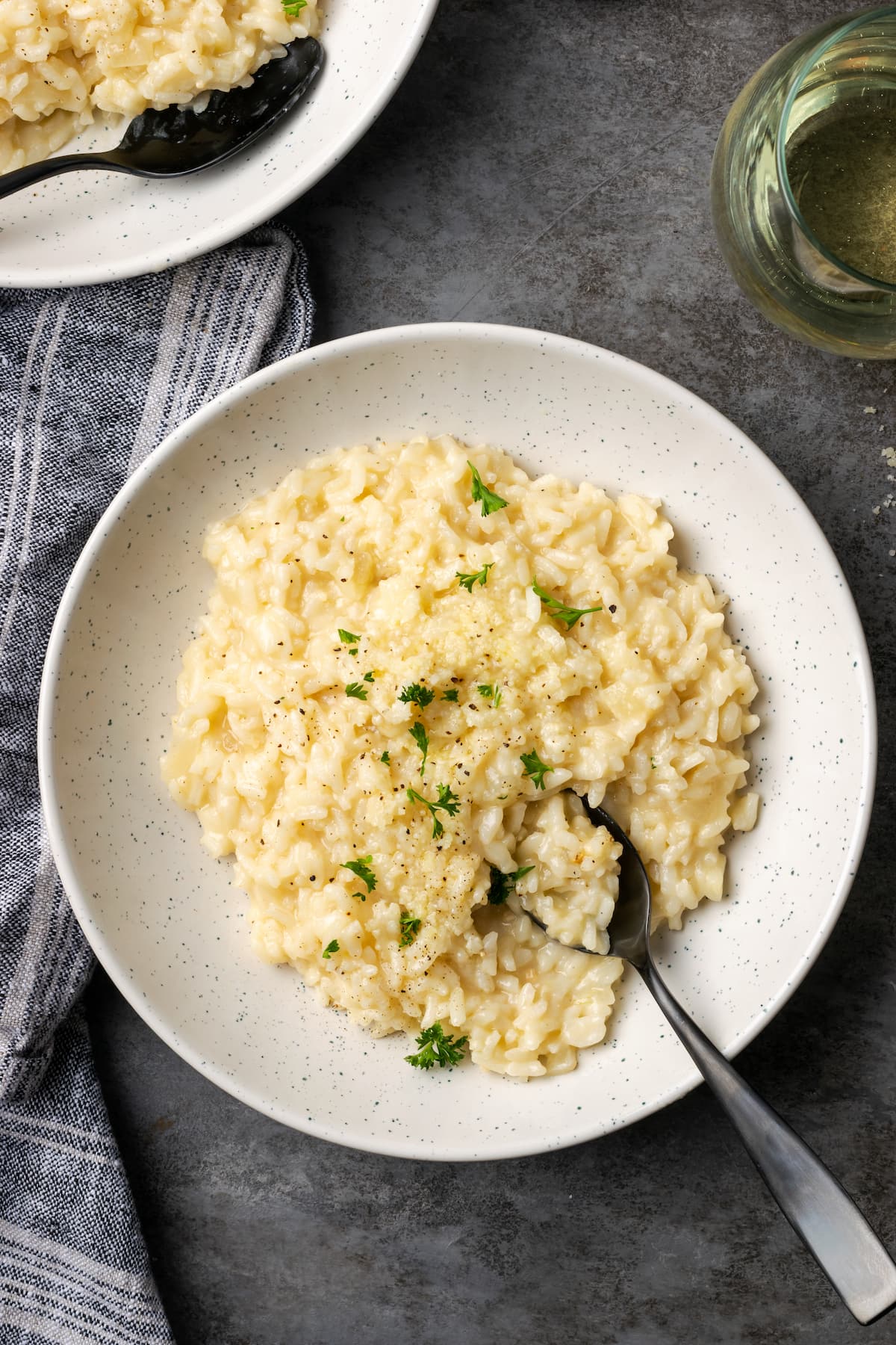 Esta receta de Instant Pot Risotto es un plato principal o guarnición fácil que es tan rico y cremoso como el risotto clásico, ¡y está listo en 30 minutos! Un tazón de risotto cremoso Instant Pot con una cuchara, adornado con perejil fresco.
