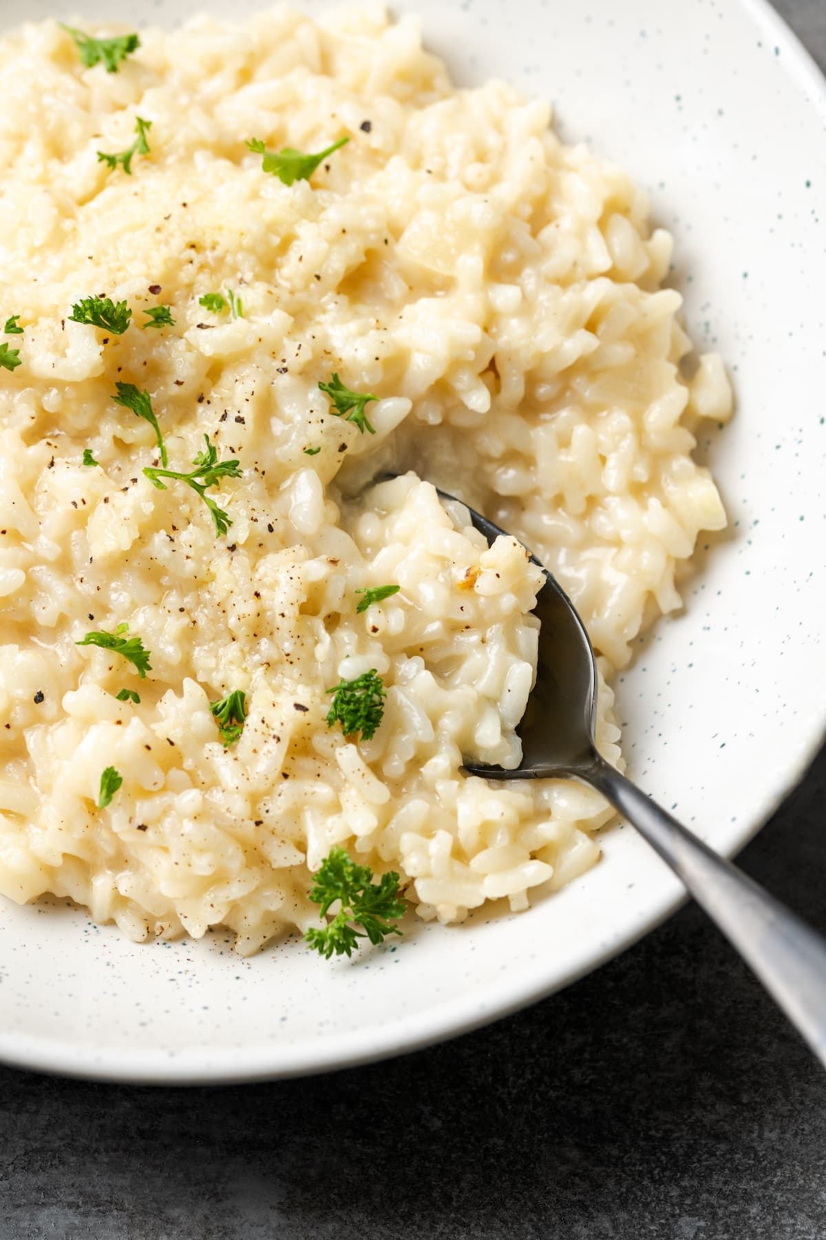 Esta receta de Instant Pot Risotto es un plato principal o guarnición fácil que es tan rico y cremoso como el risotto clásico, ¡y está listo en 30 minutos! Un tazón de risotto cremoso Instant Pot con una cuchara, adornado con perejil fresco.