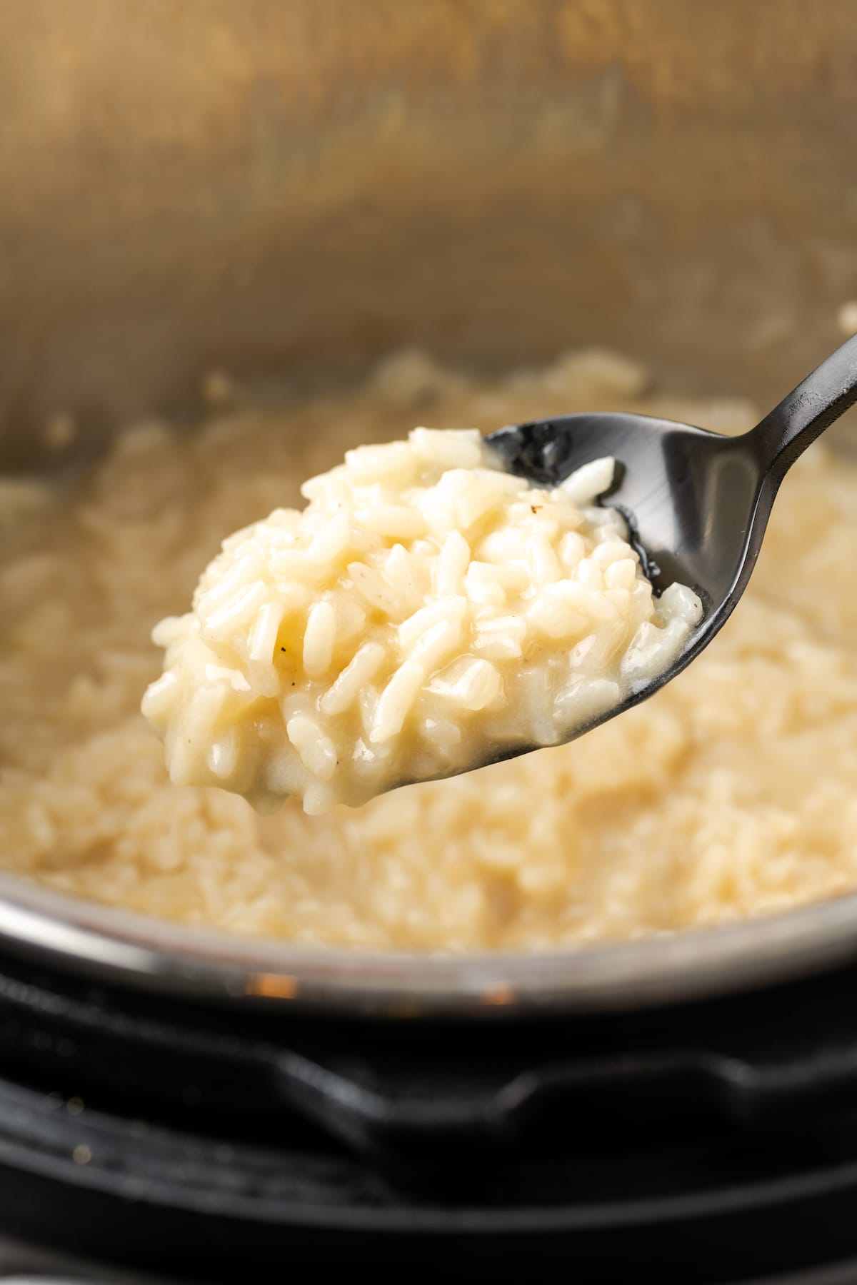 Esta receta de Instant Pot Risotto es un plato principal o guarnición fácil que es tan rico y cremoso como el risotto clásico, ¡y está listo en 30 minutos! Una cucharada de risotto Instant Pot con una olla llena de risotto en el fondo.