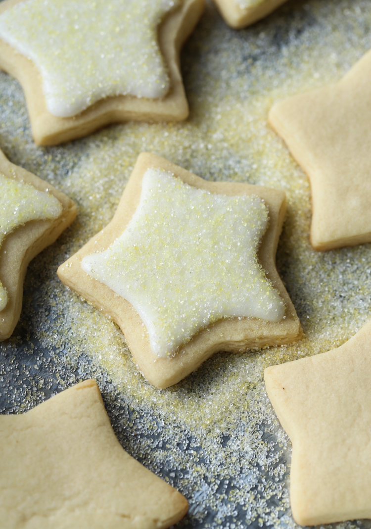 Galletas de azúcar cortadas en forma de estrella con glaseado blanco, espolvoreadas con azúcar en una encimera.